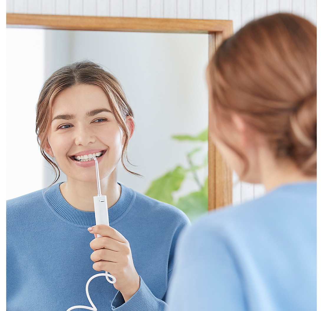 Donna sorridente usa un idropulsore davanti a uno specchio in bagno.