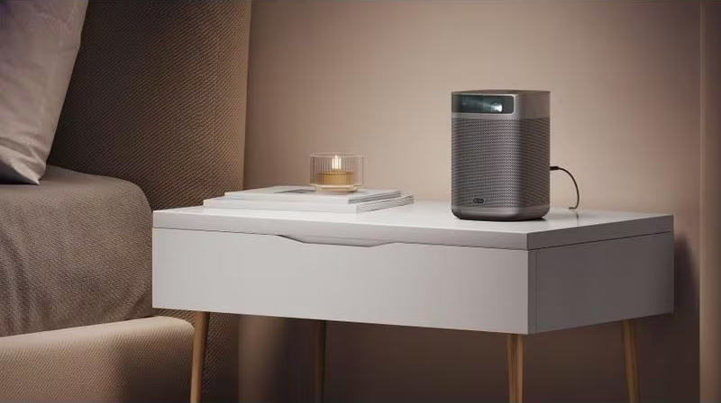 Un petit projecteur sur une table de chevet blanche à côté d'un lit.
