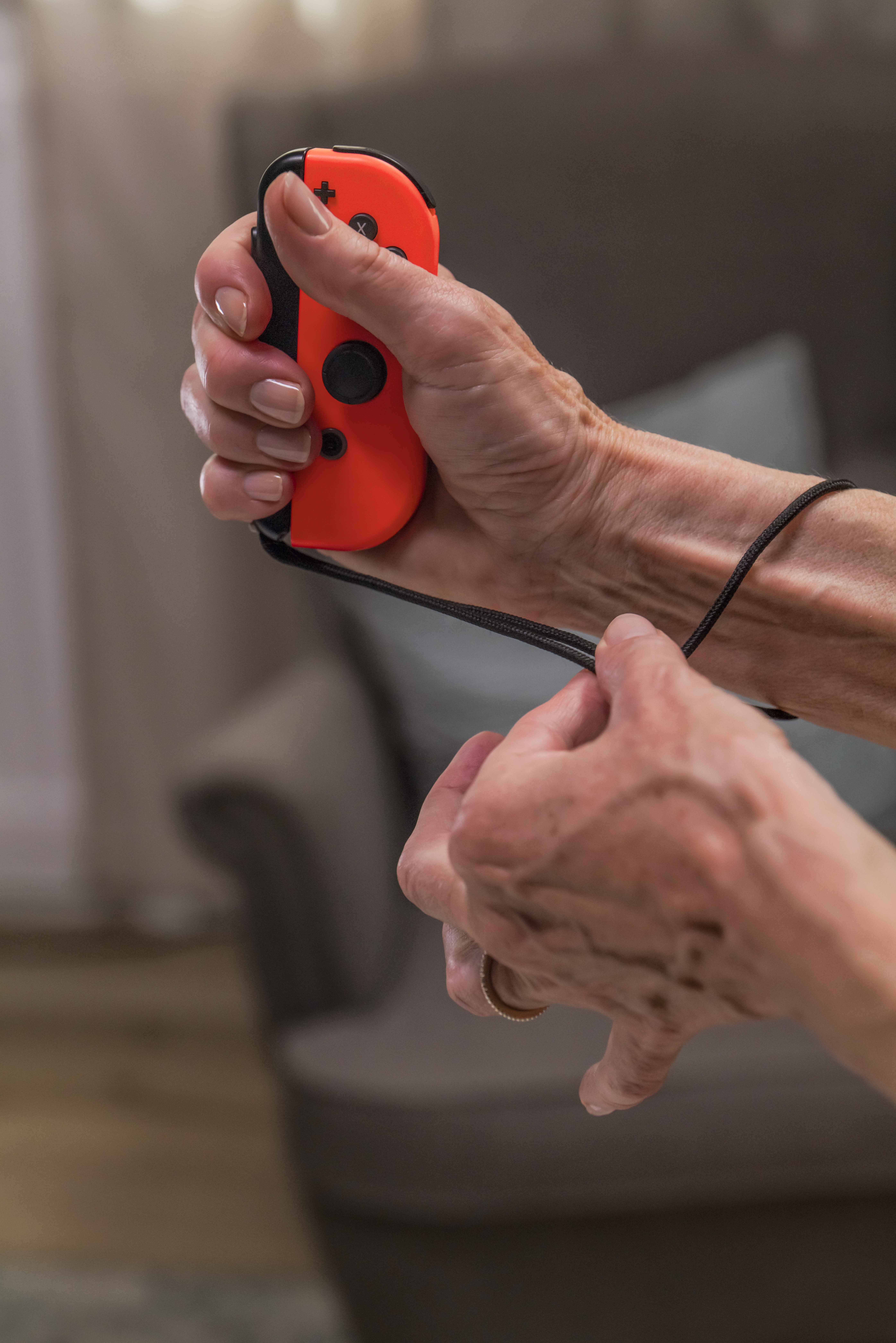 Hände halten einen orangefarbenen und schwarzen Nintendo Switch-Controller, Handschlaufe sichtbar.