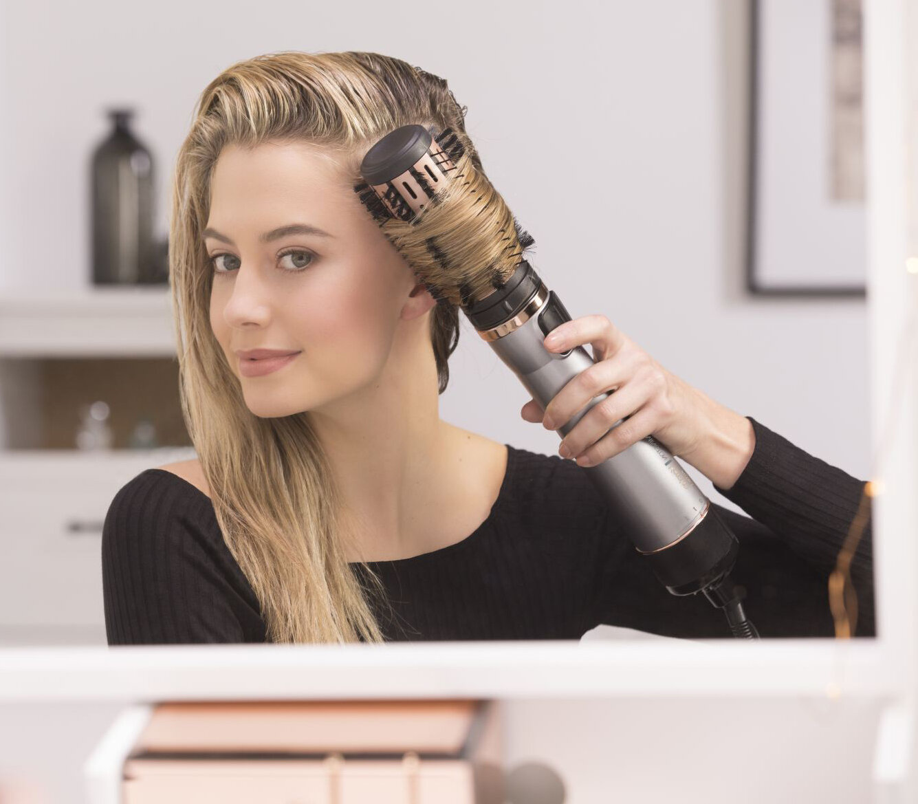 Kobieta suszy włosy obrotową szczotką, patrząc w lustro.