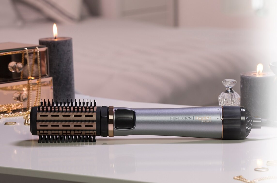 Prostownica do włosów na białym stole z świecami i biżuterią.