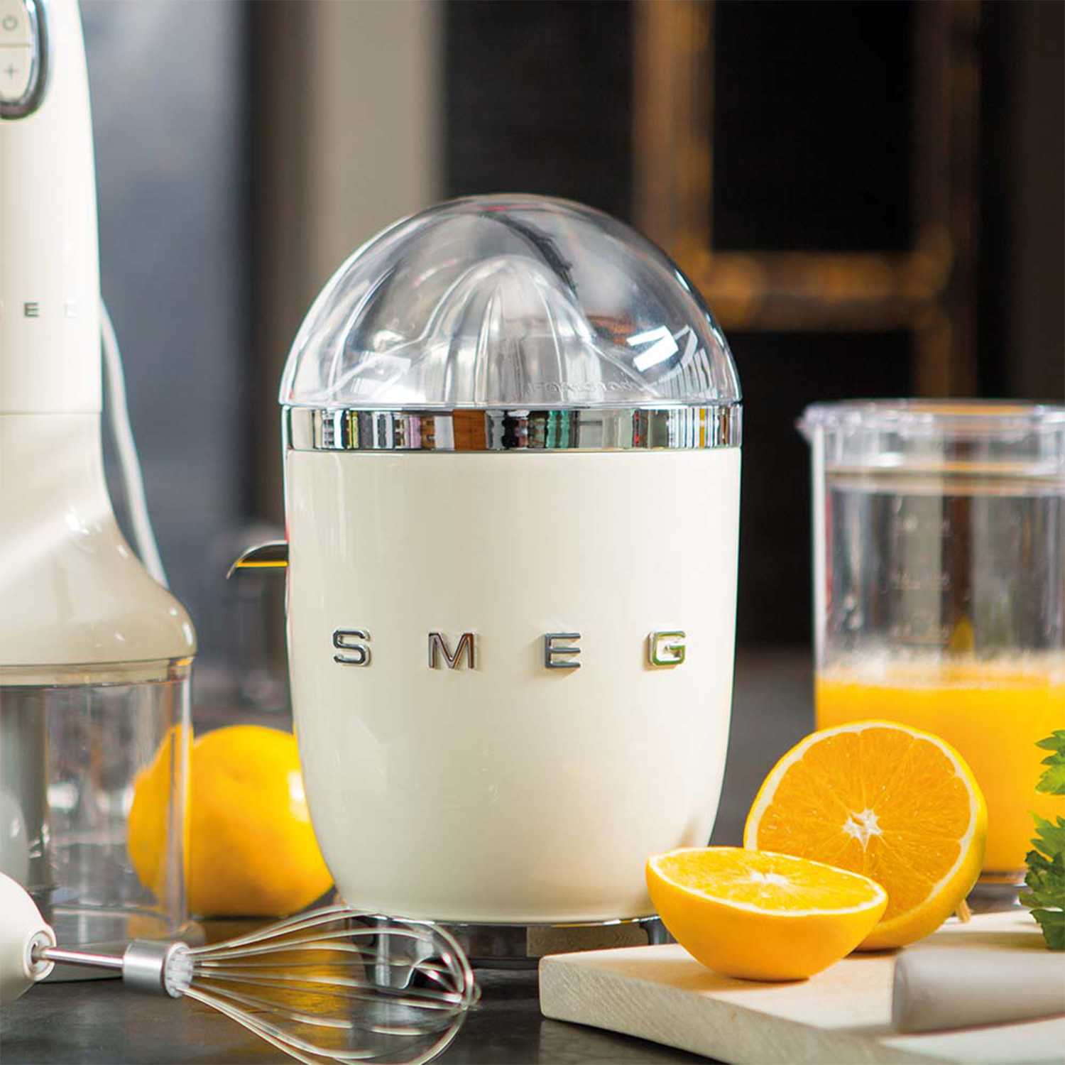 Spremiagrumi SMEG color crema con arance e limoni su un tagliere di legno.