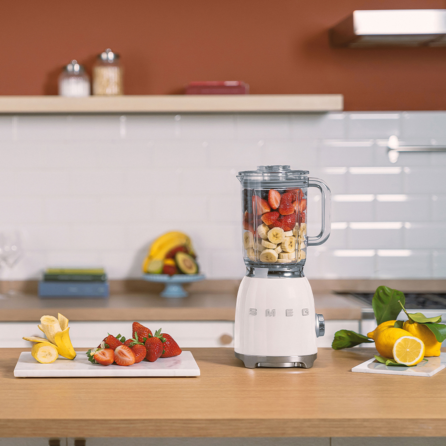 Frullatore con frutta, fragole, banane e limoni su una superficie di legno.