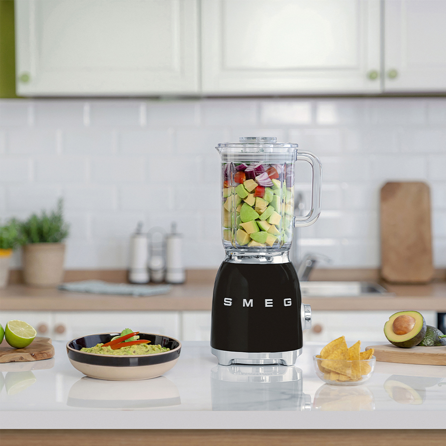Frullatore con frutta e verdura all'interno. Guacamole e patatine su un tavolo con lime.