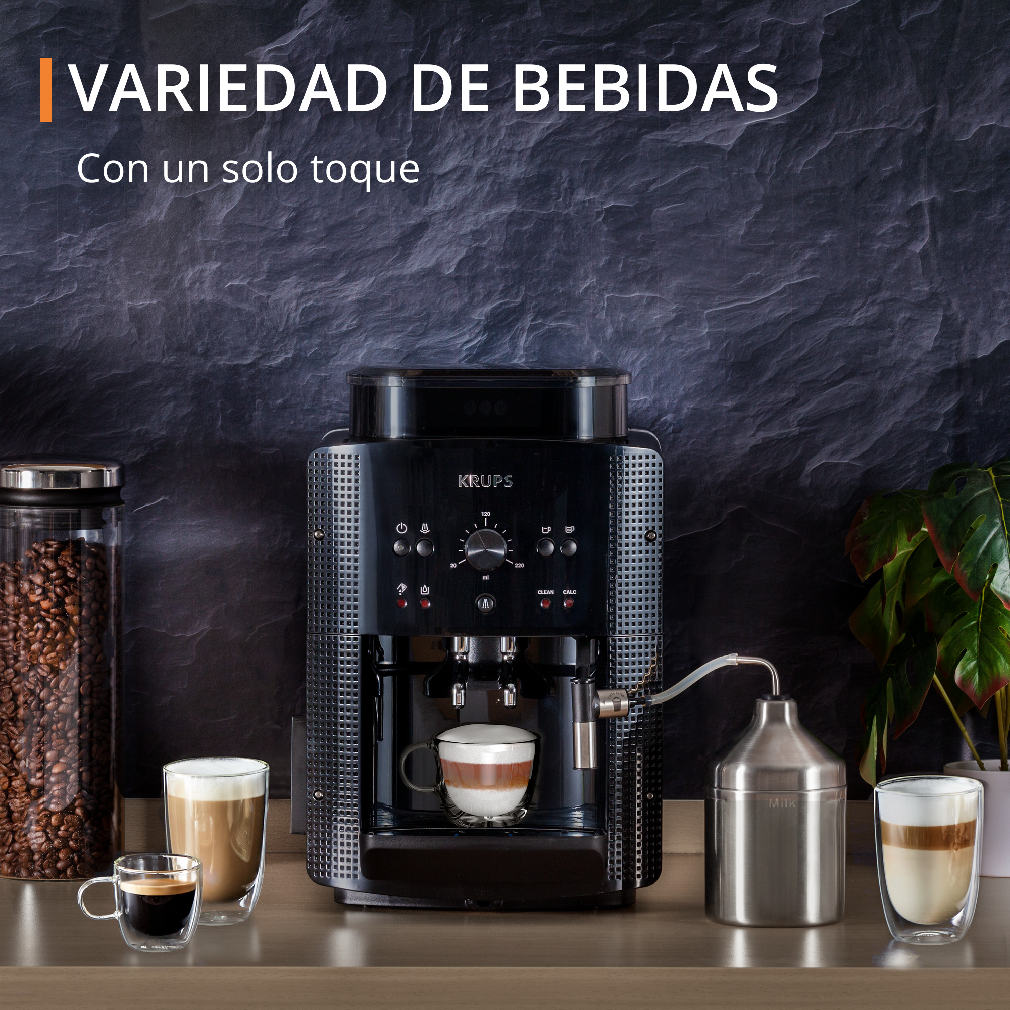 Cafetera Krups negra, dos tazas de café y un recipiente de leche al lado.