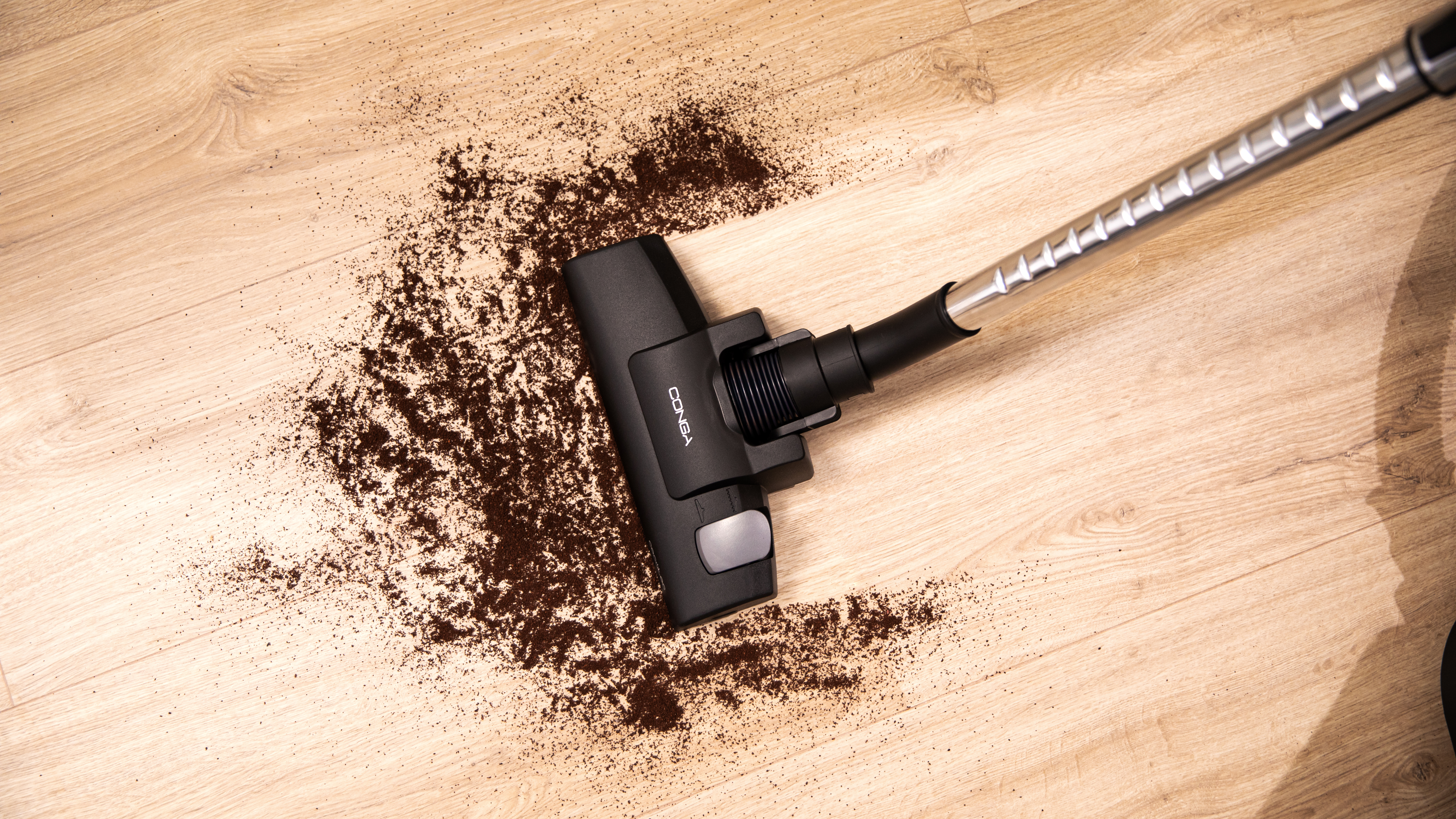 Cabezal de aspiradora en suelo de madera con posos de café esparcidos.