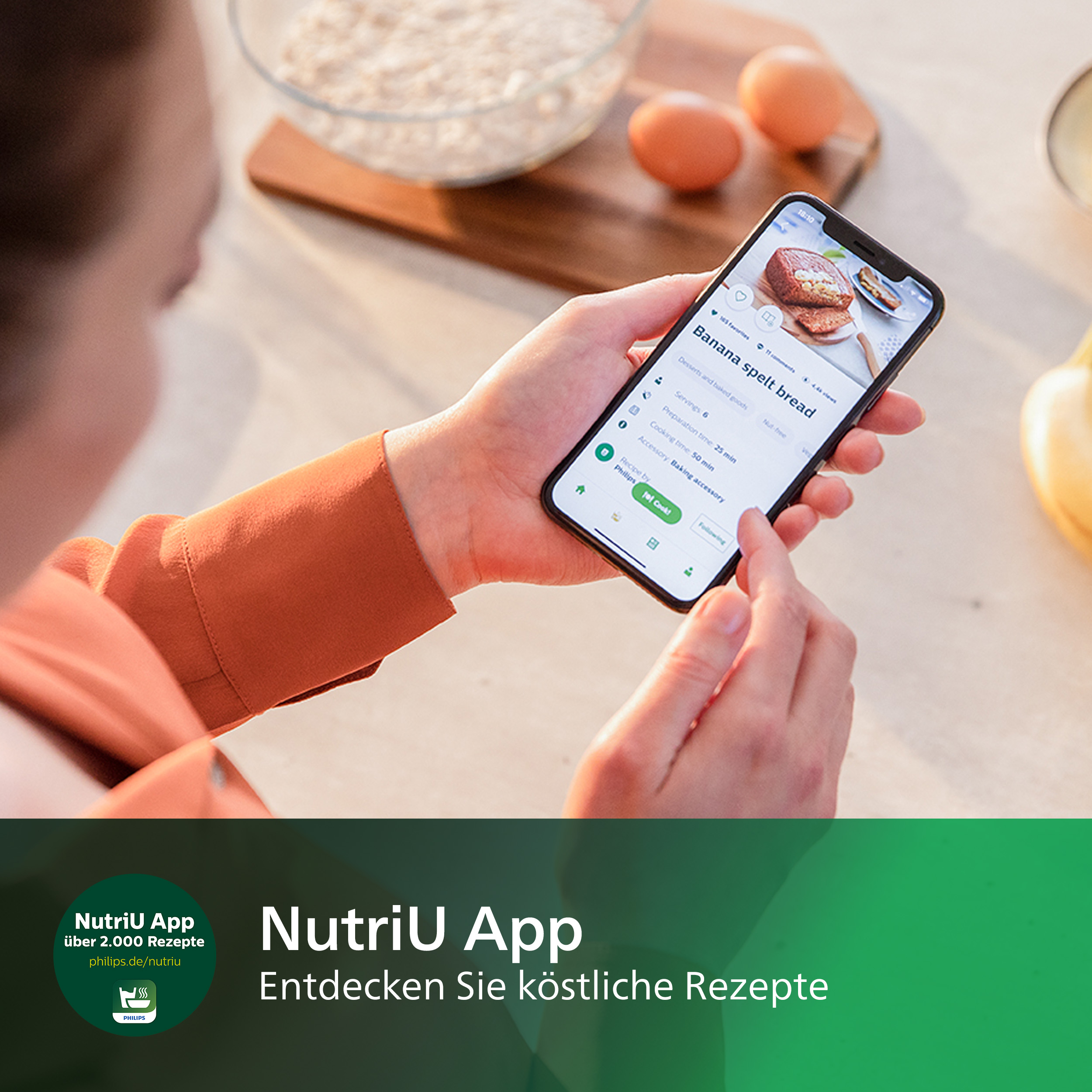 Eine Person, die ein Telefon mit einem Rezept für Bananen-Dinkelbrot hält. Eier und andere Zutaten sind sichtbar.