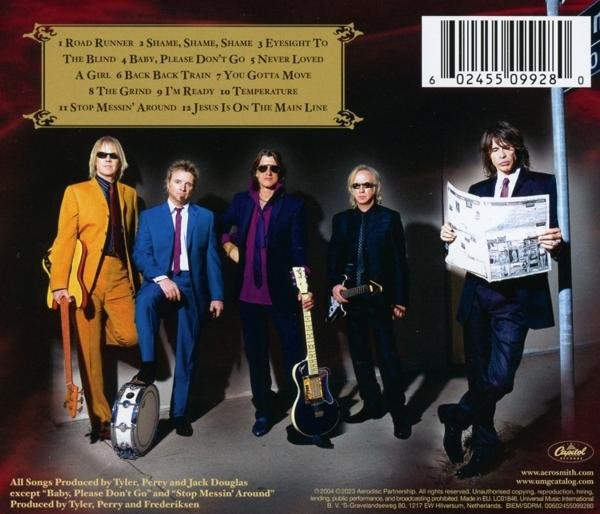 Aerosmith-Bandmitglieder in einem Gruppenfoto. Sie stehen vor einer Backsteinmauer und halten Instrumente.