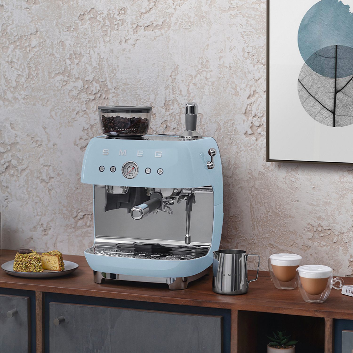 Macchina per espresso SMEG azzurra, con tazza e lattiera su un bancone in legno.