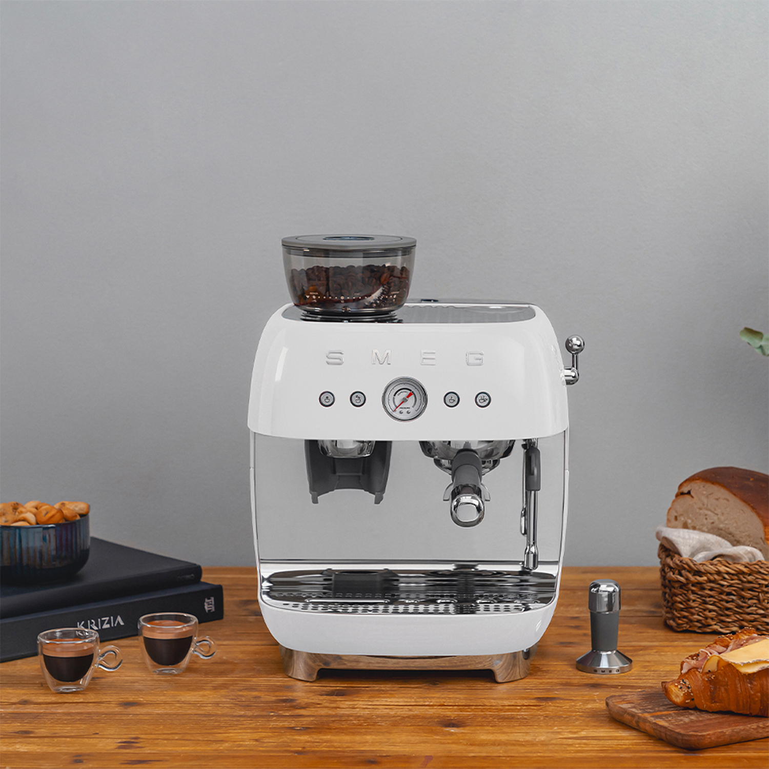 Macchina per espresso SMEG bianca con accessori su un tavolo di legno. Sfondo grigio.