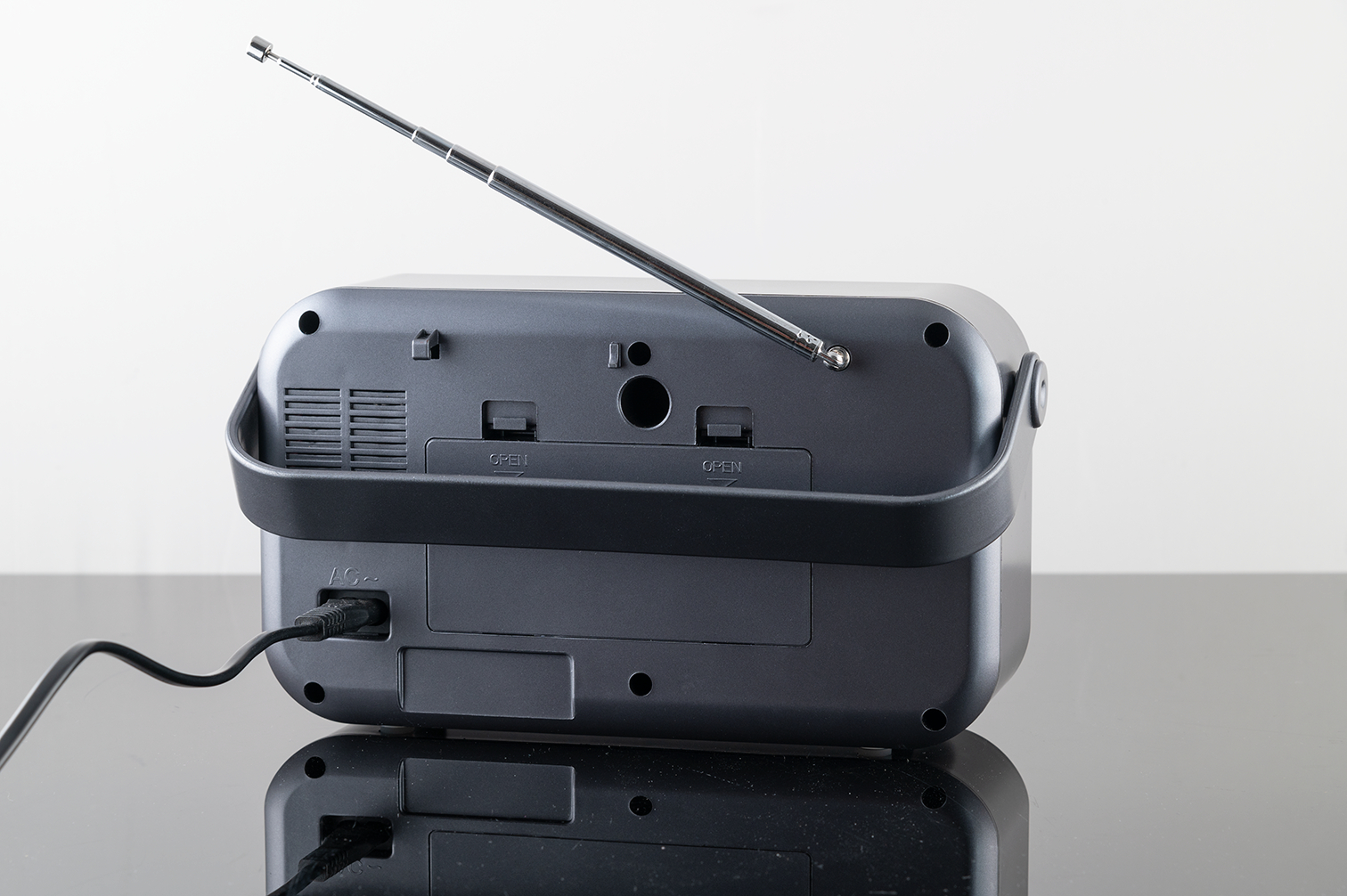 Rückseite eines grauen tragbaren Radios auf schwarzer Oberfläche. Zeigt Antenne und Netzkabel.