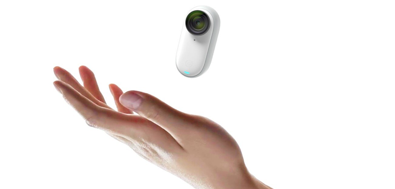 Ręka trzymająca mały biały aparat z zielonym obiektywem.