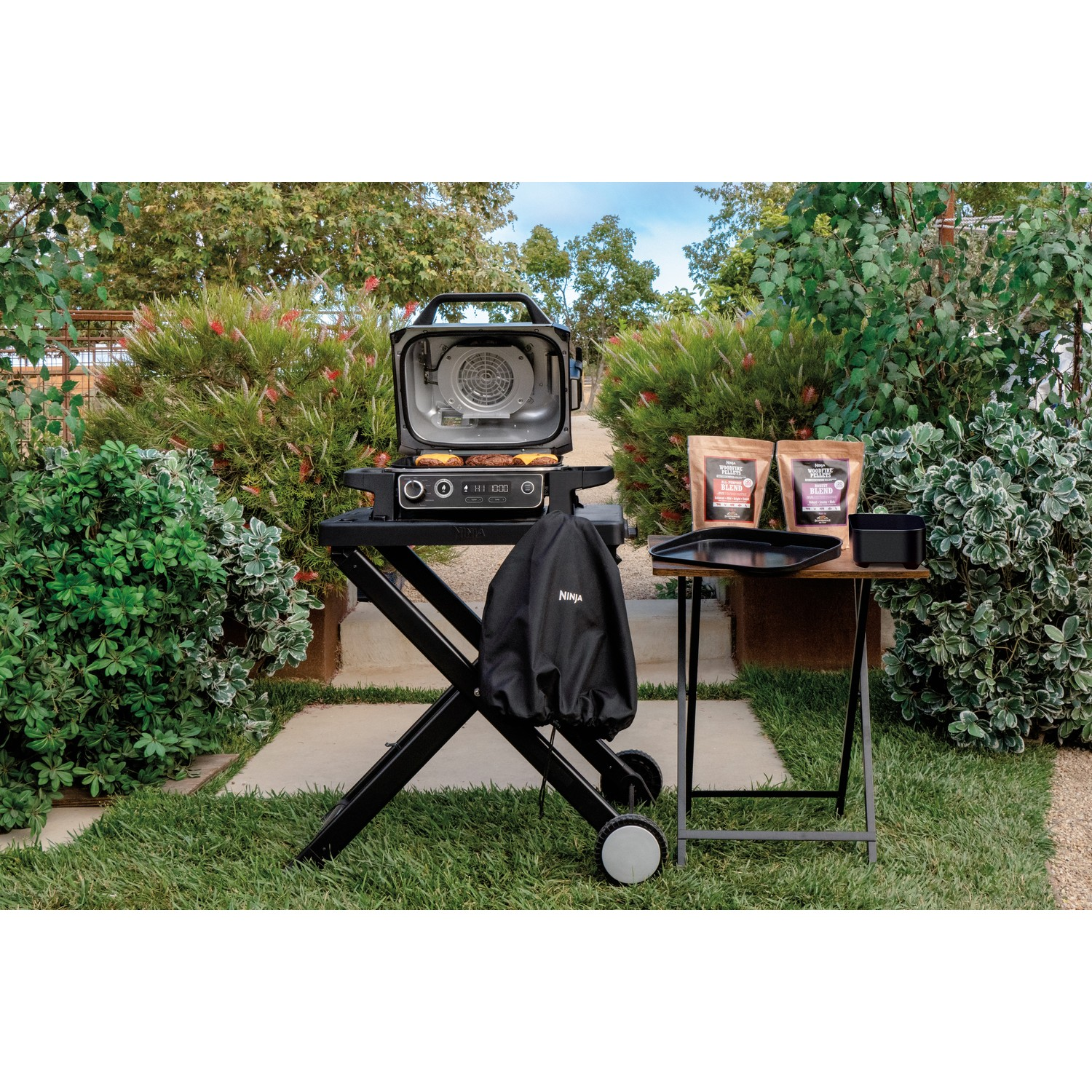 Buitengrill op een kar, met een hoes en een bijzettafel met grillaccessoires.