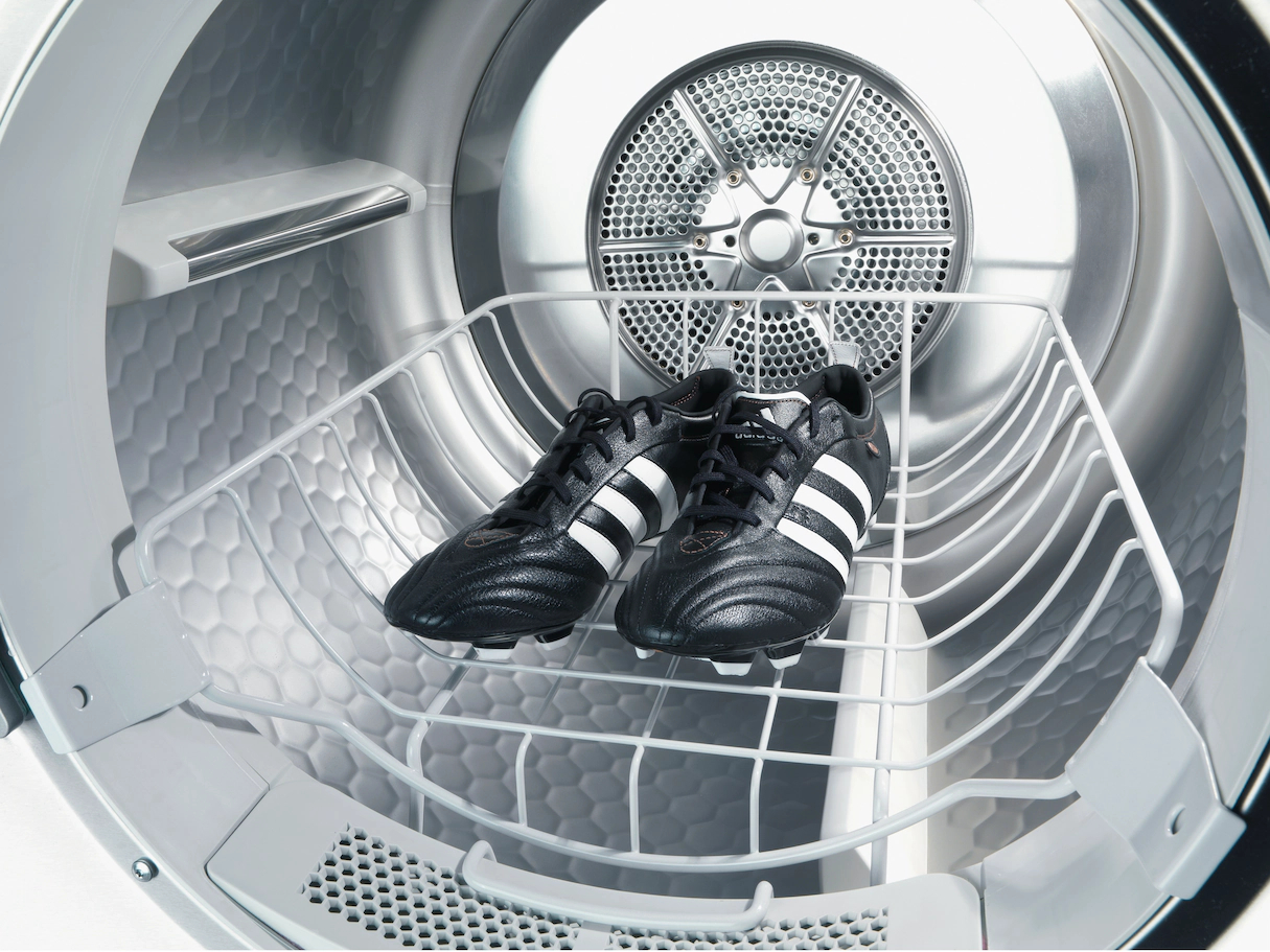 Ein weißer Trocknerinnenraum mit einem Gestell mit schwarz-weißen Fußballschuhen.
