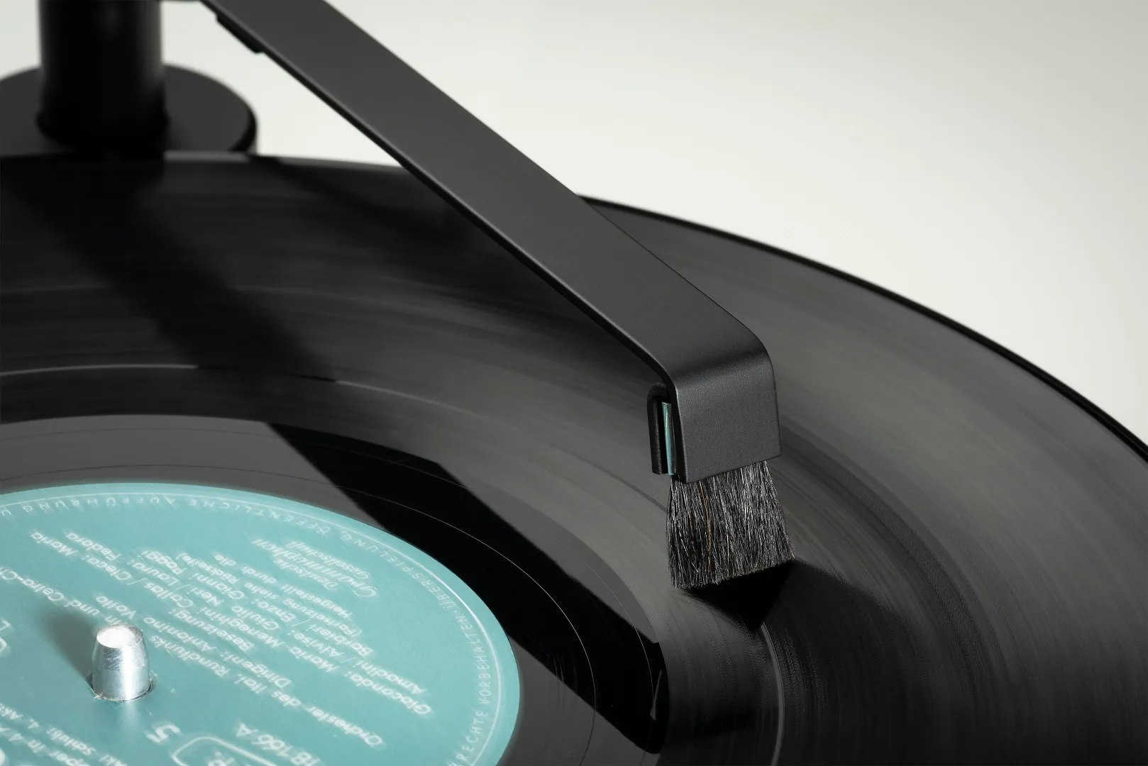 Ein schwarzer Plattenreiniger bürstet eine Vinylplatte ab. Die Bürste reinigt die Rillen.