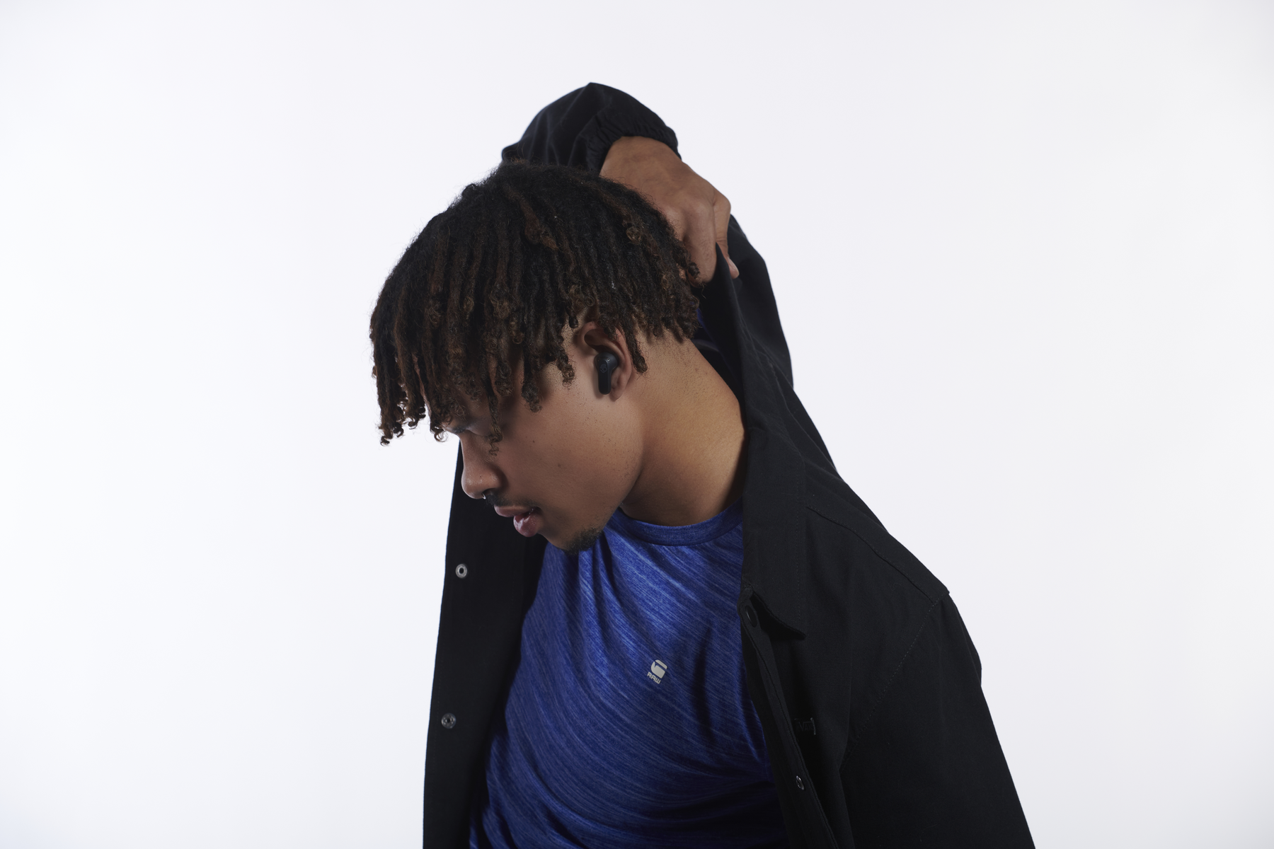 Dreadlock-os férfi kék ingben és fekete dzsekiben, lefelé nézve.