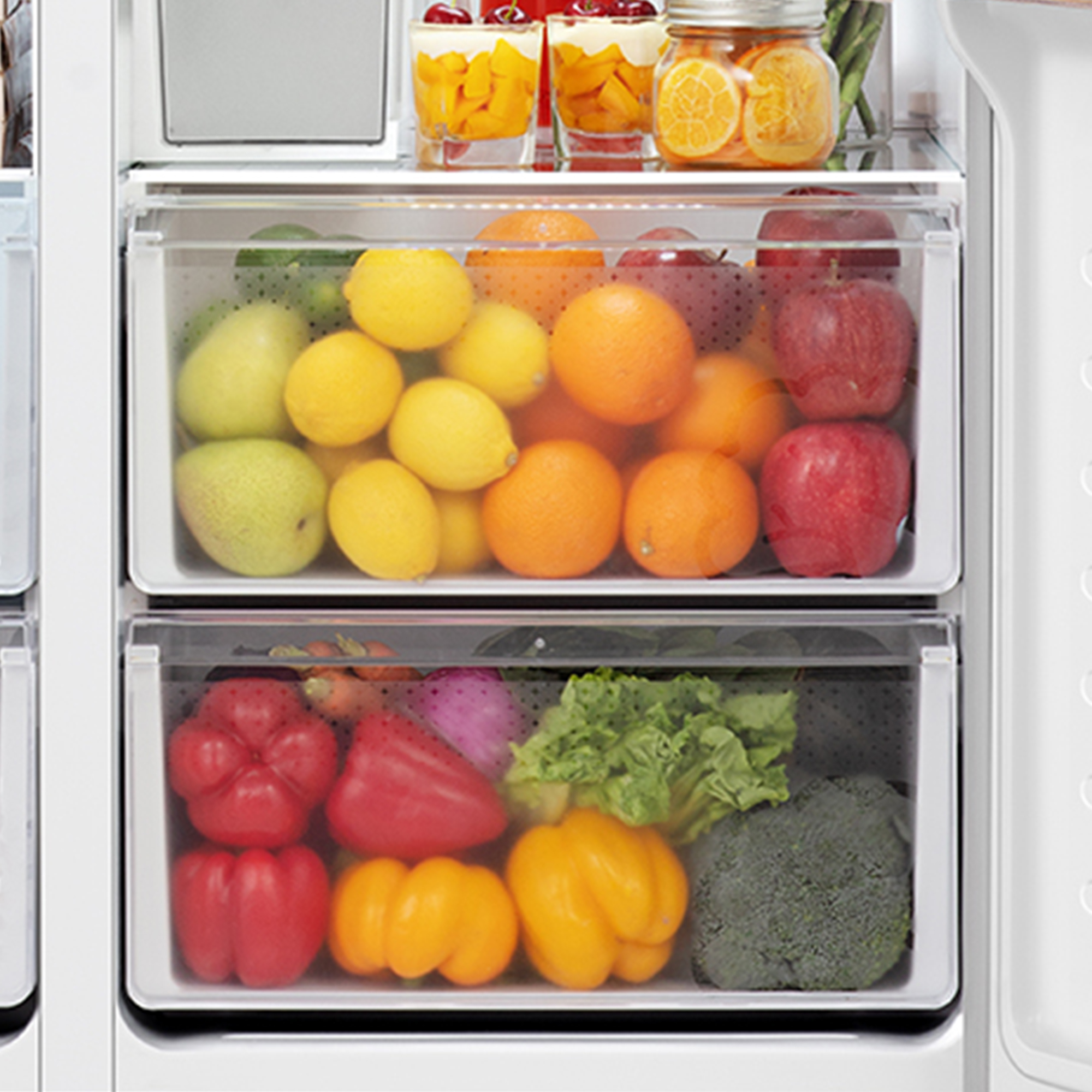 Dentro de un refrigerador, se ven cajones llenos de frutas y verduras. Naranjas, manzanas, brócoli.