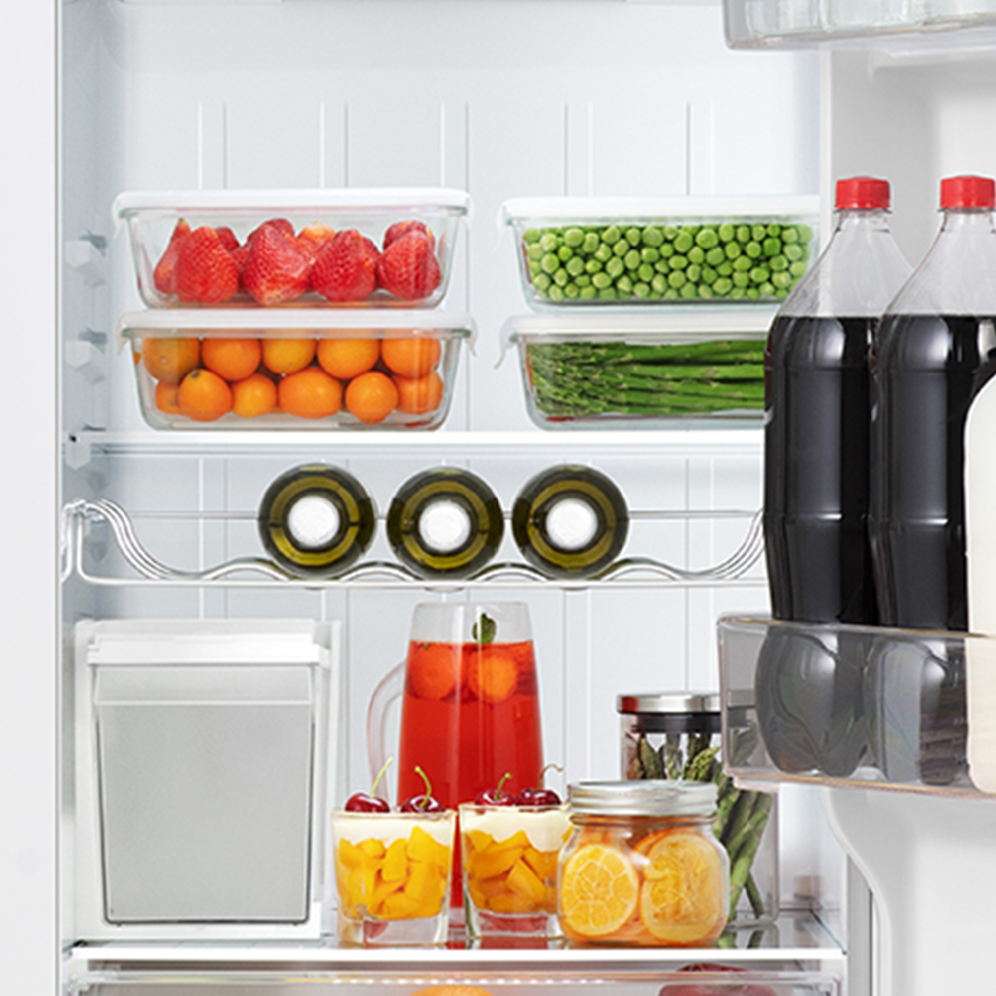 Interior de nevera con fresas, guisantes, naranjas, botellas, tarros y postres en vasos.