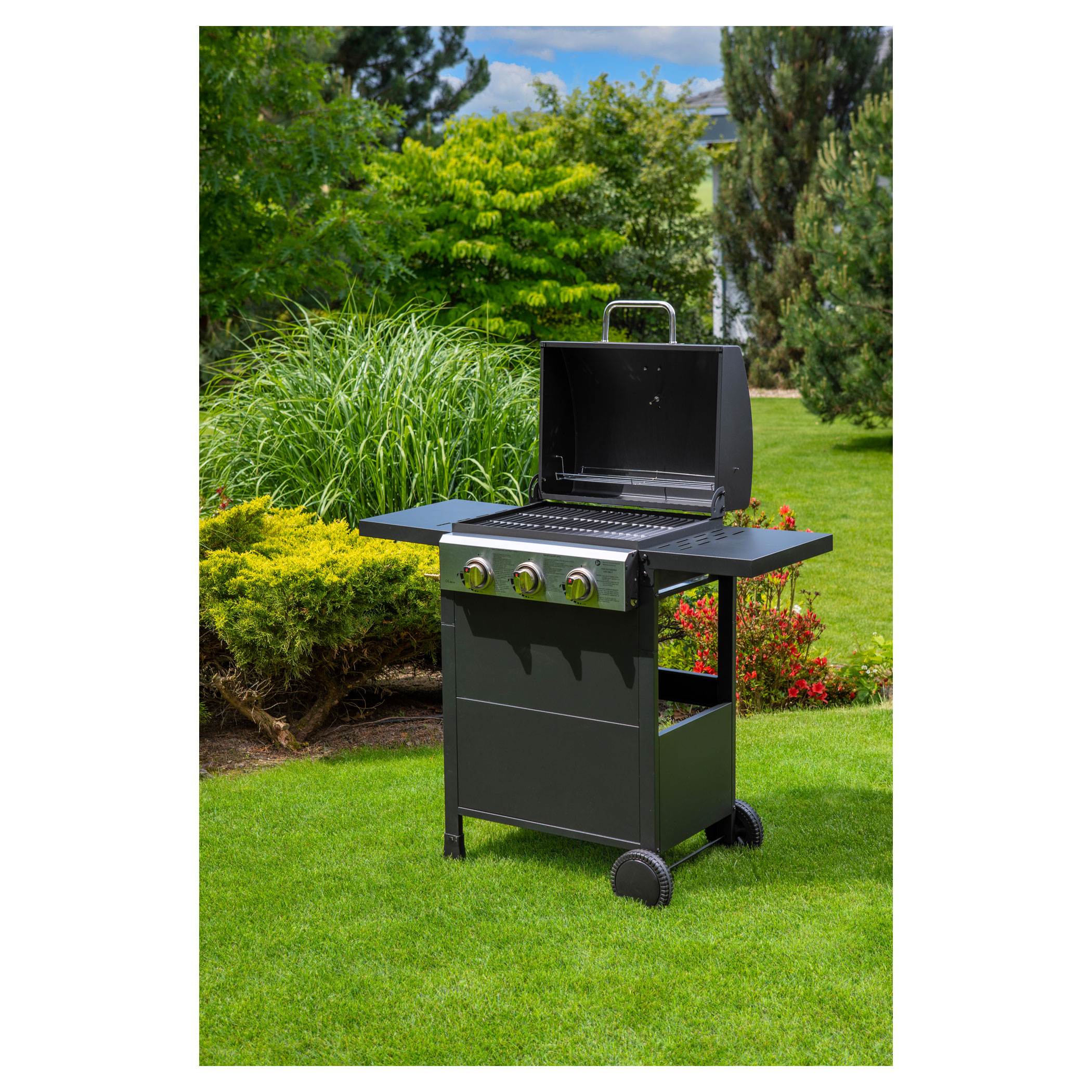 Egy fekete grill a zöld gyepen, bokrokkal és fákkal körülvéve egy kerti környezetben.