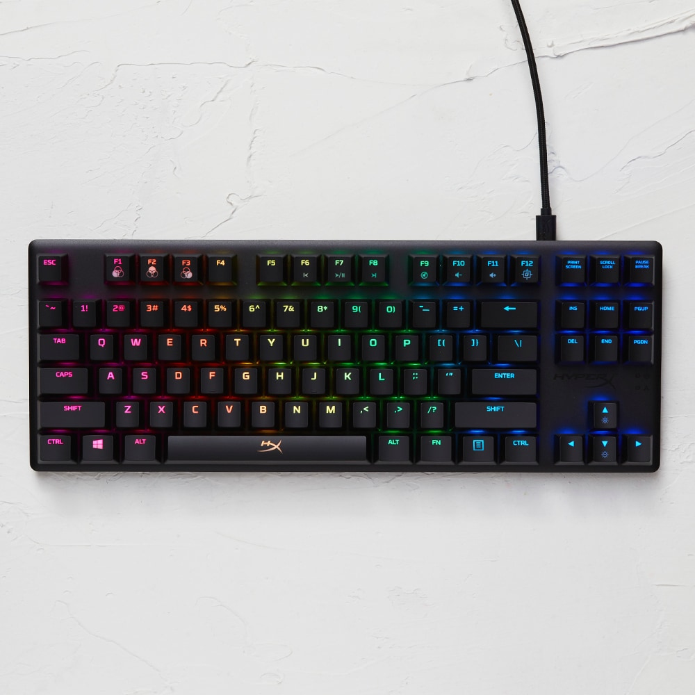 Schwarze Gaming-Tastatur mit beleuchteten Tasten, mehrfarbig, auf weißer Oberfläche.