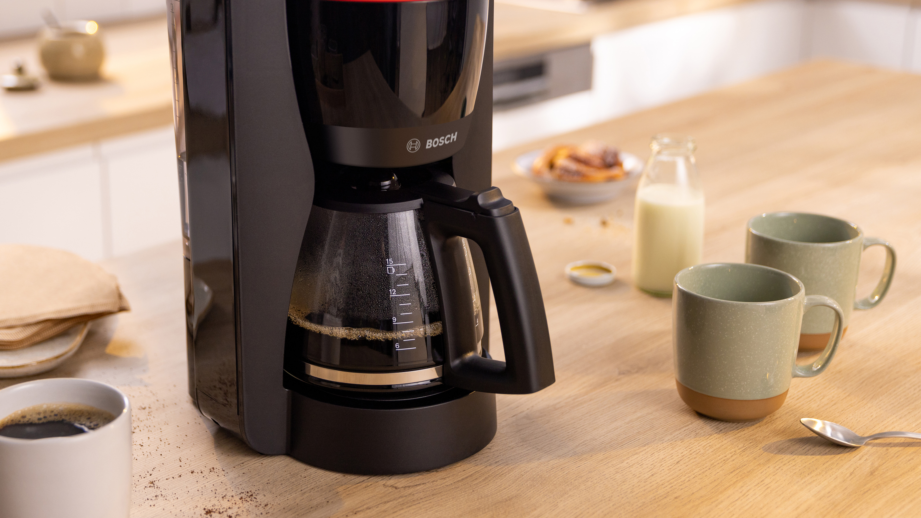Eine Kaffeemaschine auf einem Holztisch mit Tassen, Milch und Gebäck.