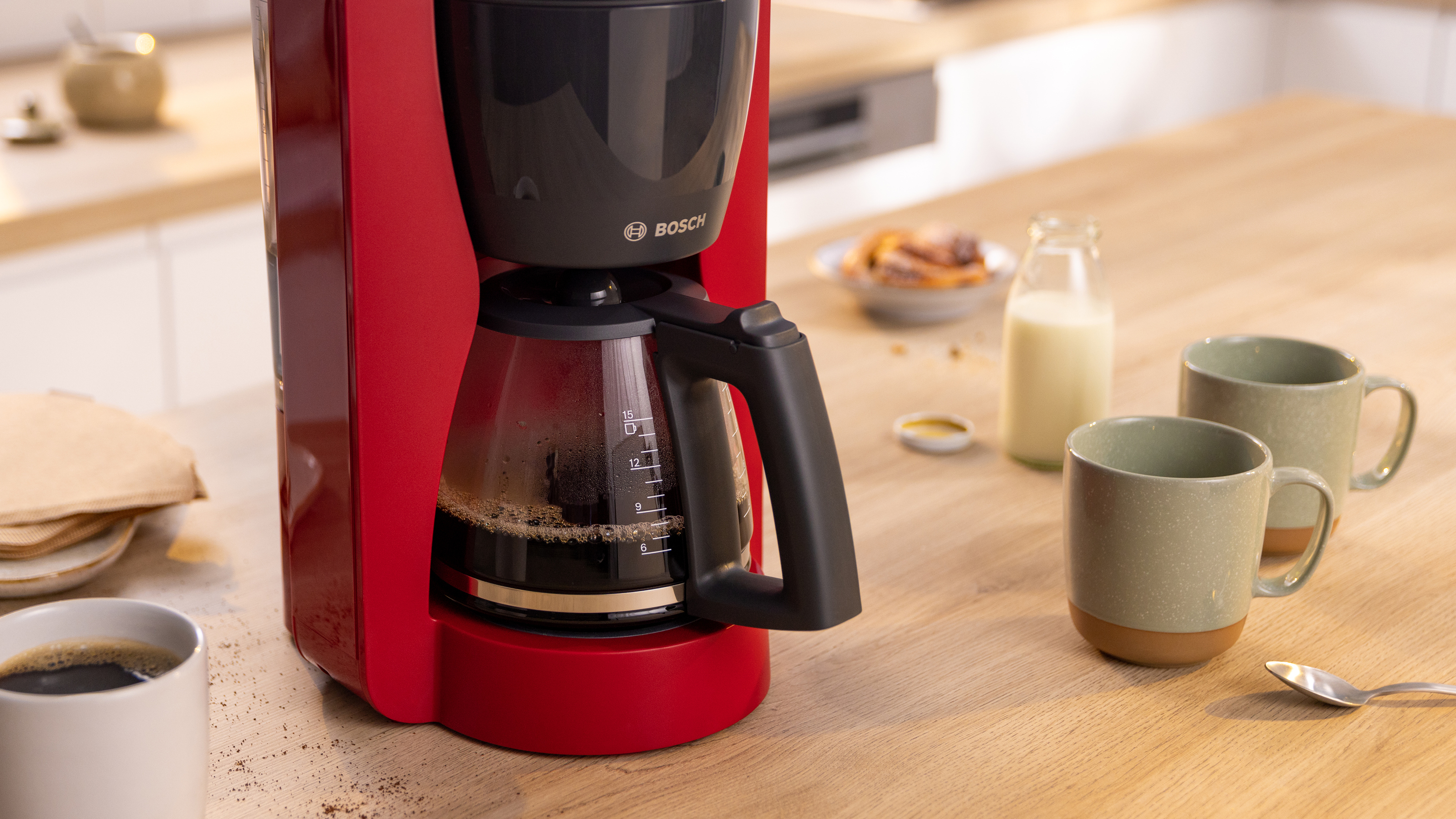 Roter Kaffeemaschine auf einem Holztisch mit Kaffee, Tassen, Milch und Gebäck.