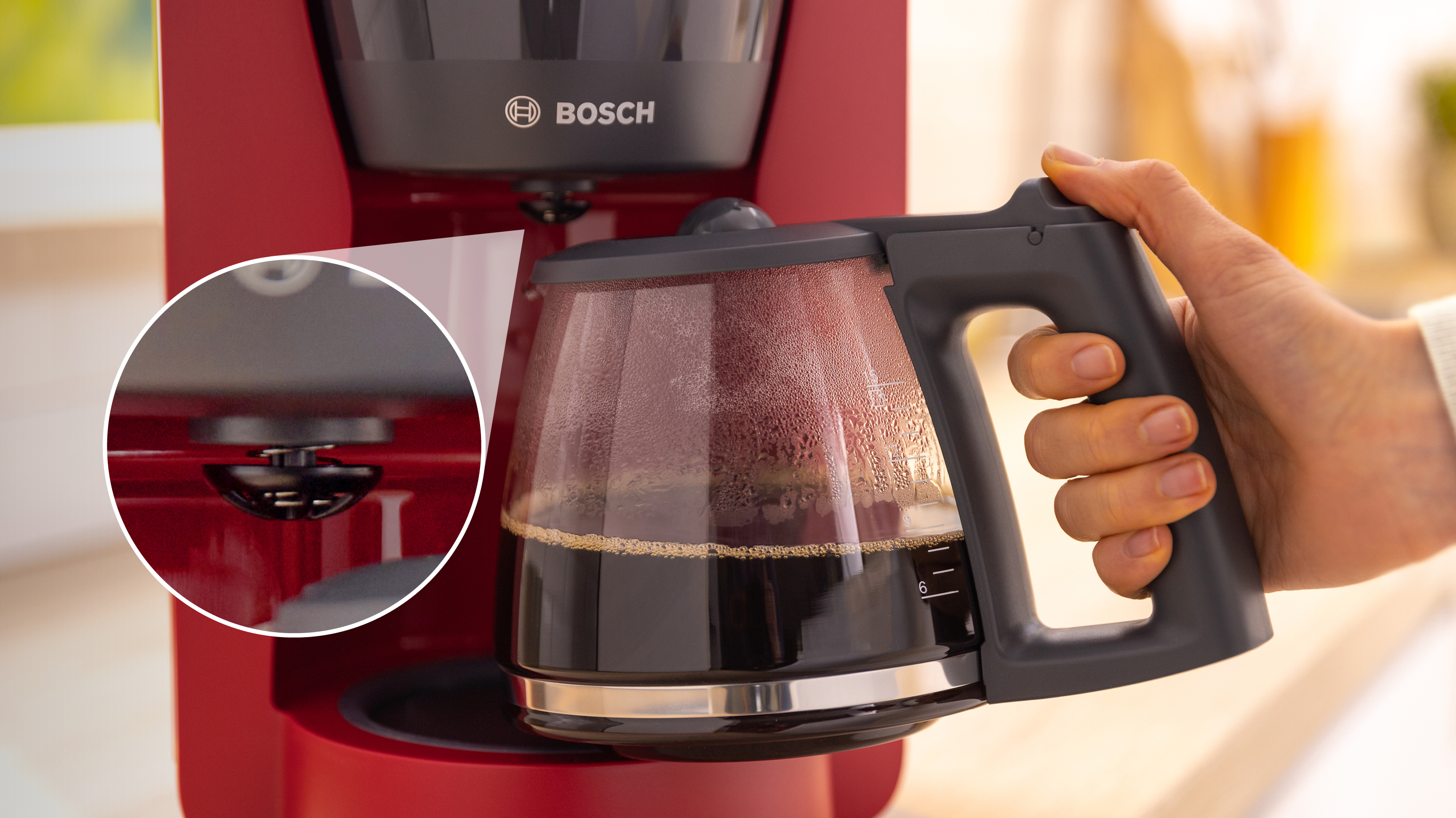 Eine rote Kaffeemaschine, eine Hand hält die Glaskaraffe mit Kaffee gefüllt.