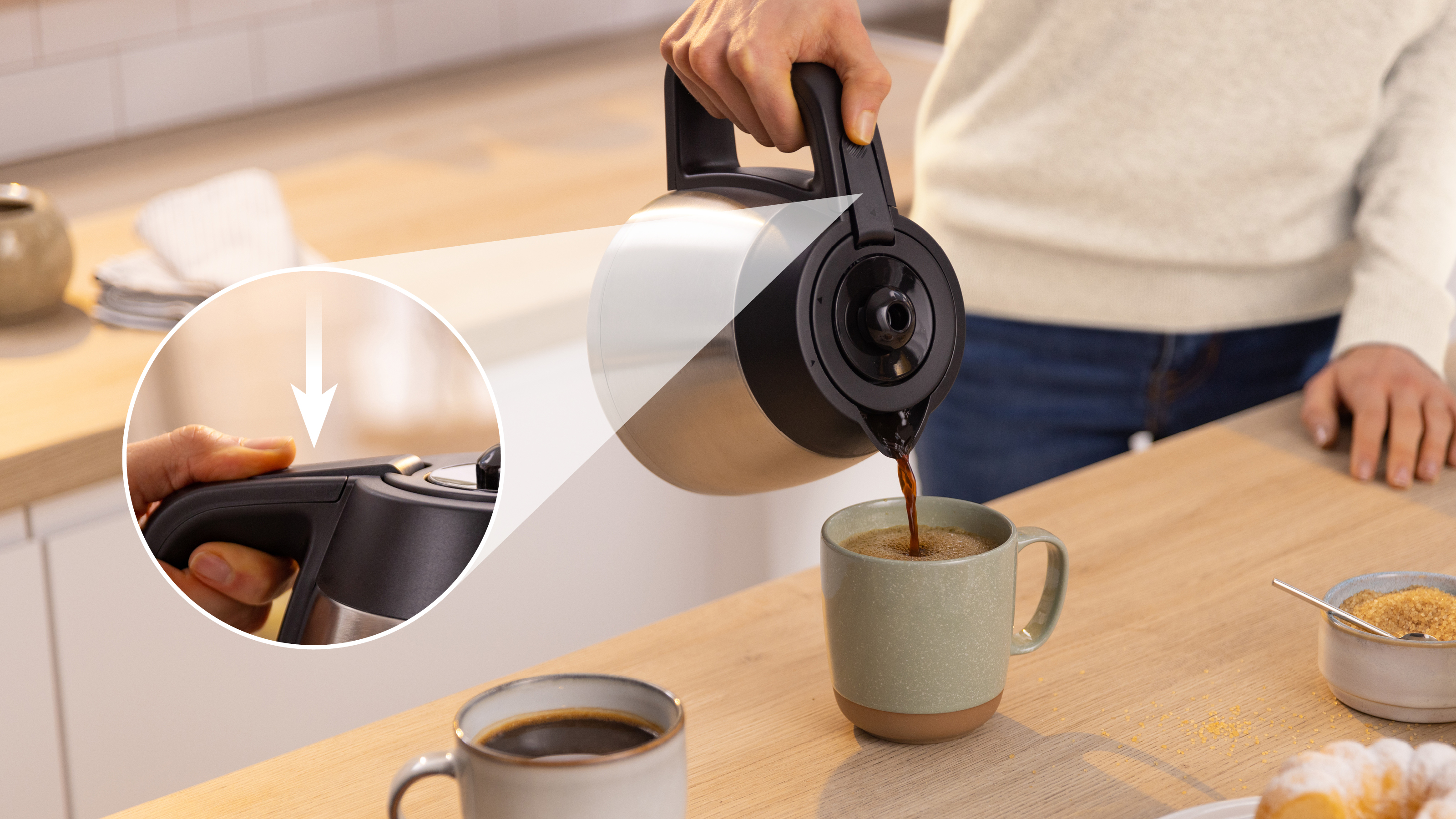 Eine Person gießt Kaffee aus einer silbernen und schwarzen Kaffeekanne in eine Tasse.