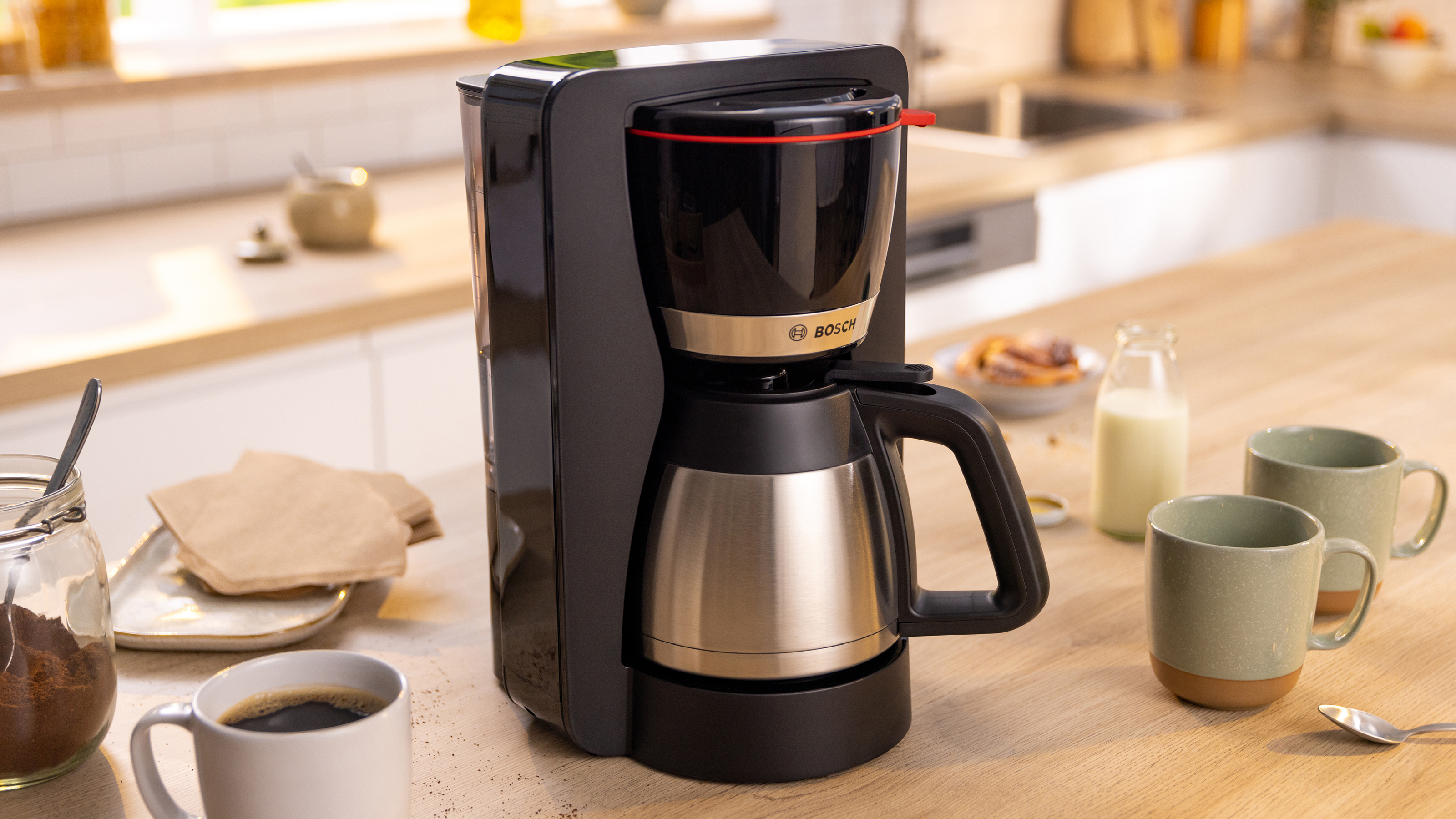 Schwarze und silberne Kaffeemaschine auf einer Holztheke. Es gibt Kaffee, Tassen und verwandte Artikel.
