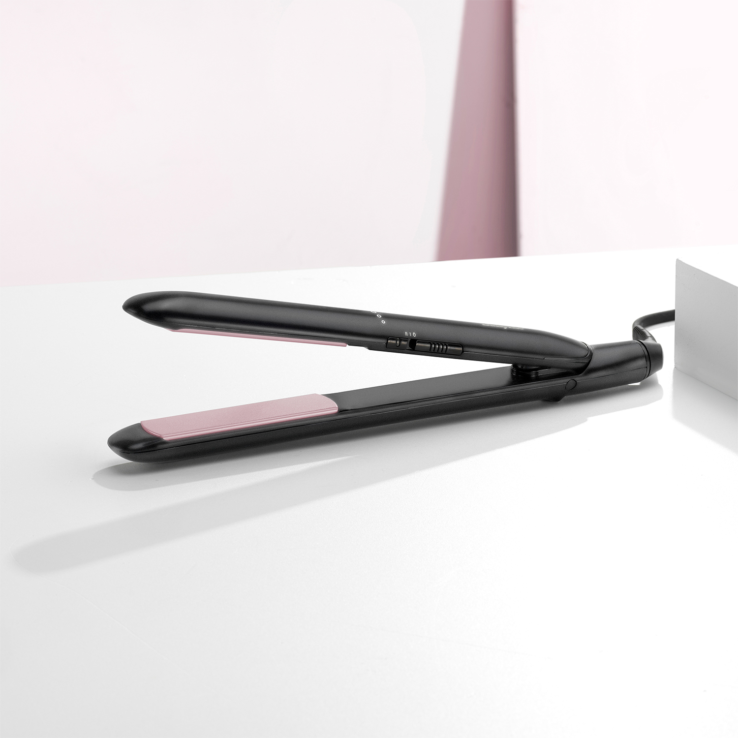 Piastra per capelli nera su superficie bianca. Piastre riscaldanti rosa aperte. Sfondo bianco e rosa.