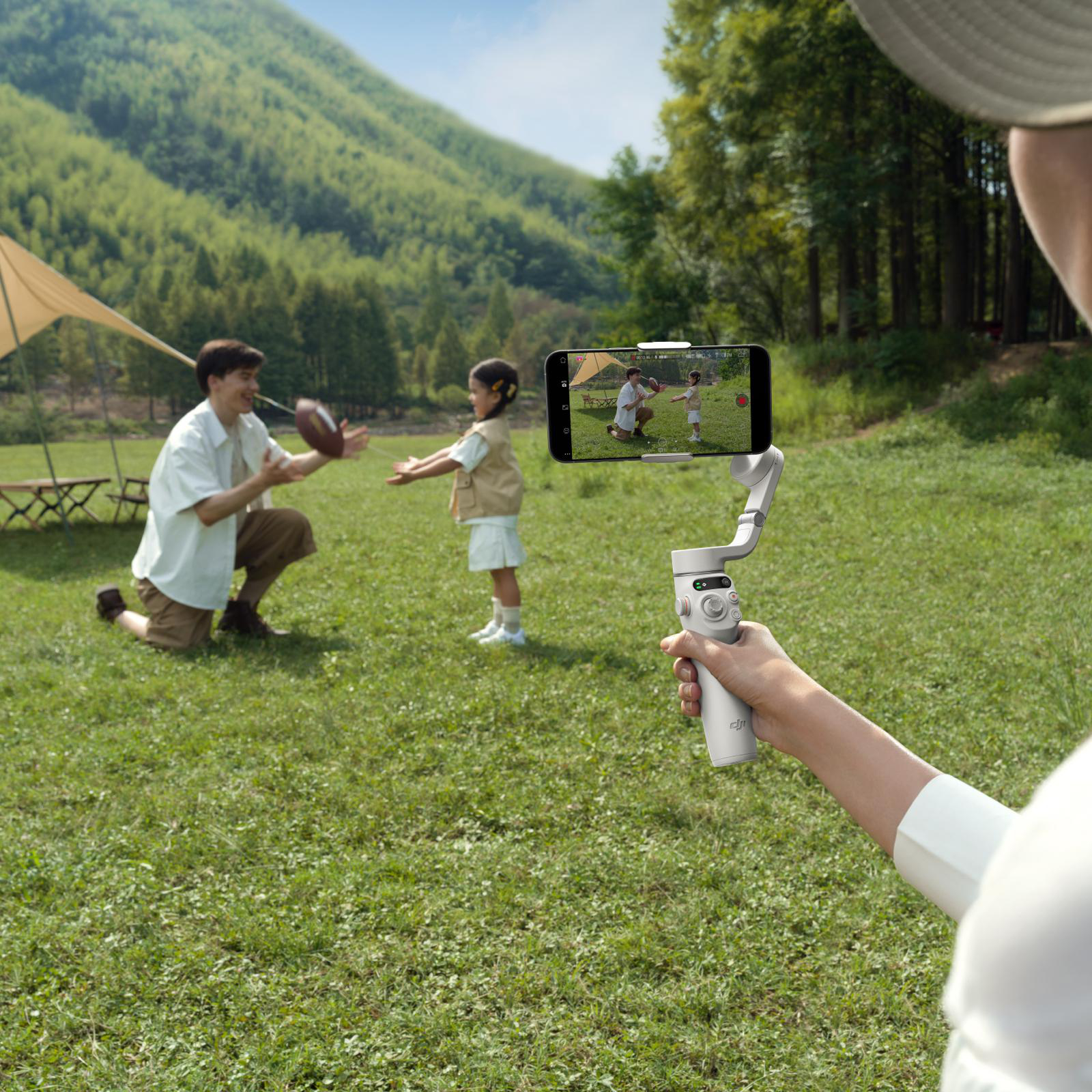 Eine Person filmt eine Familie, die mit einem Fußball auf einem Feld spielt, mit einem Telefon.