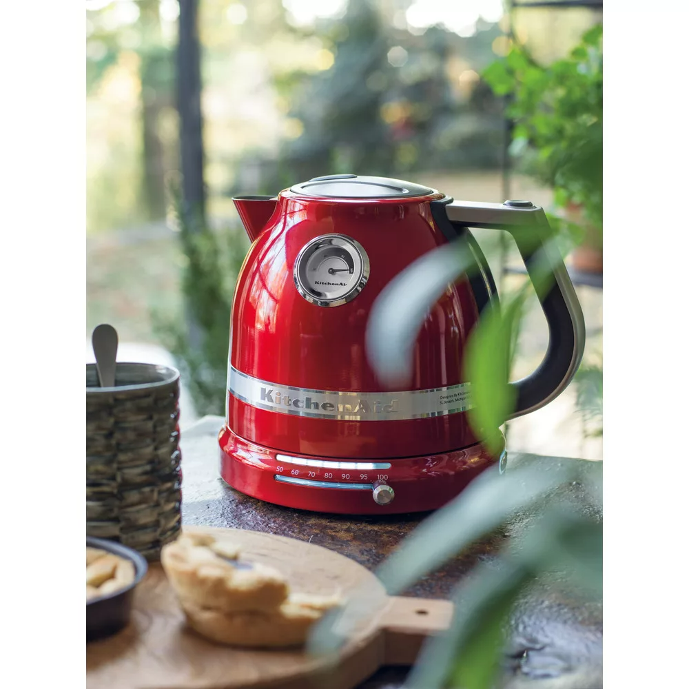 Piros KitchenAid vízforraló asztalon. Pite, csésze kanállal és zöld a háttérben. Kültéri környezet.