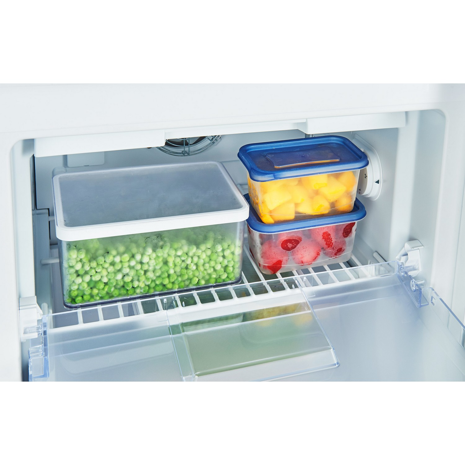 Refrigerator interior with containers of peas, mangoes, and strawberries.