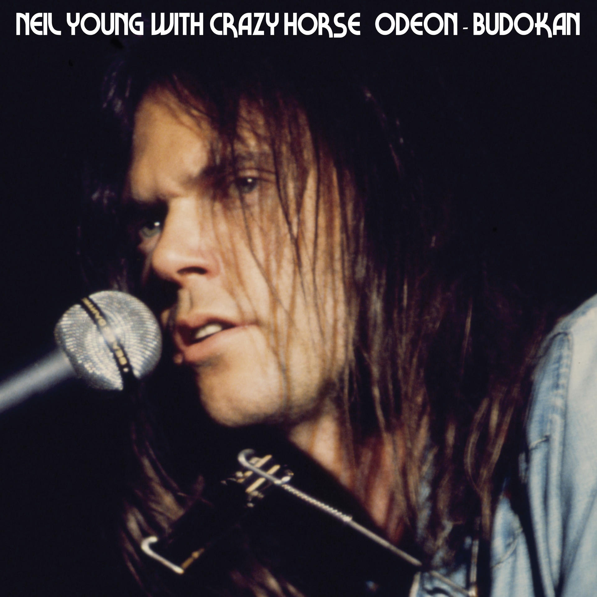 Neil Young met Crazy Horse op het podium, met een microfoon en harmonica.