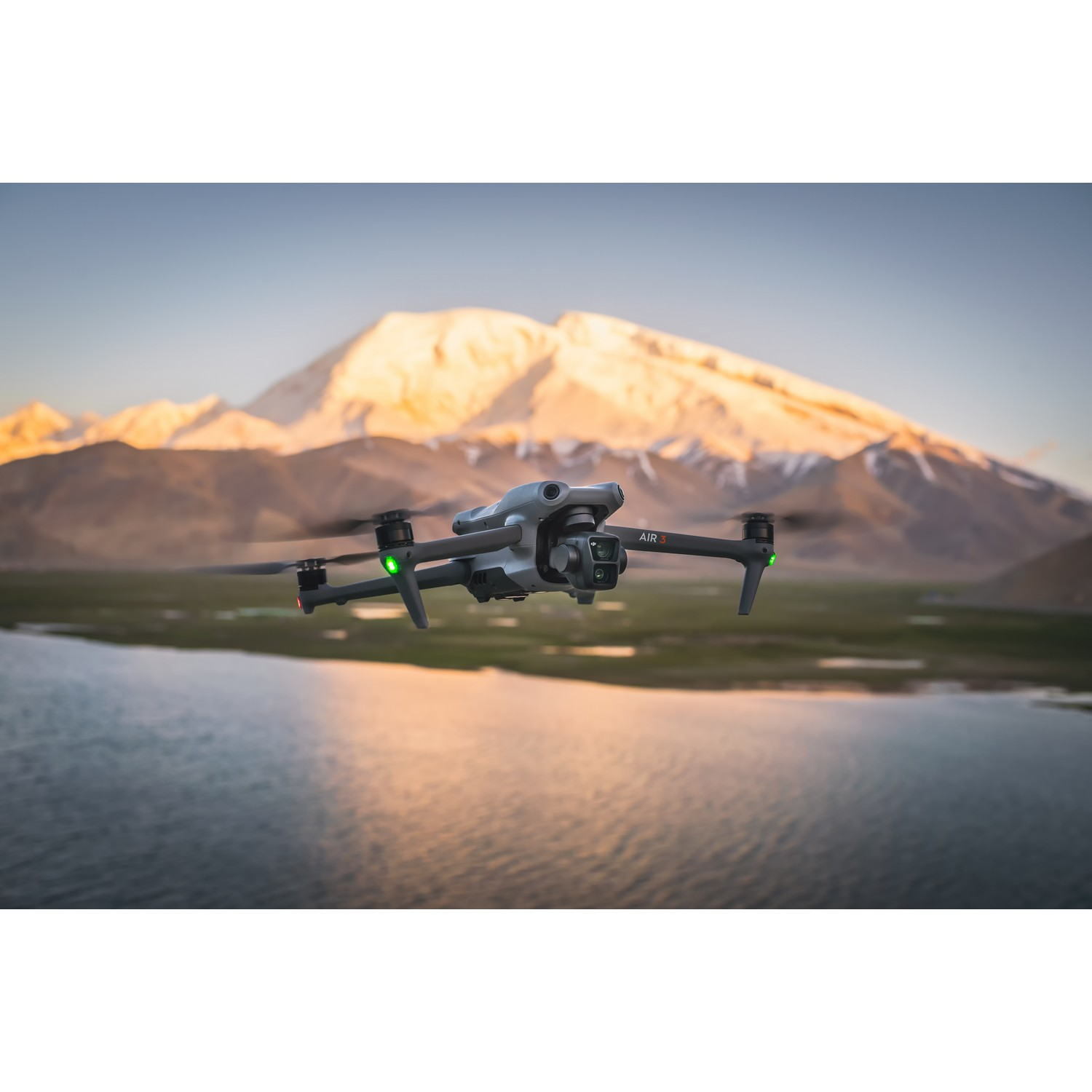 Een drone die over een meer vliegt met bergen op de achtergrond bij zonsondergang.