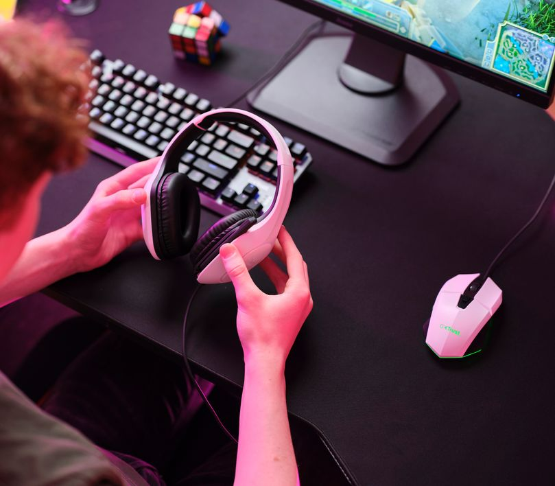Személy fehér fejhallgatót és rózsaszín gamer egeret tart.