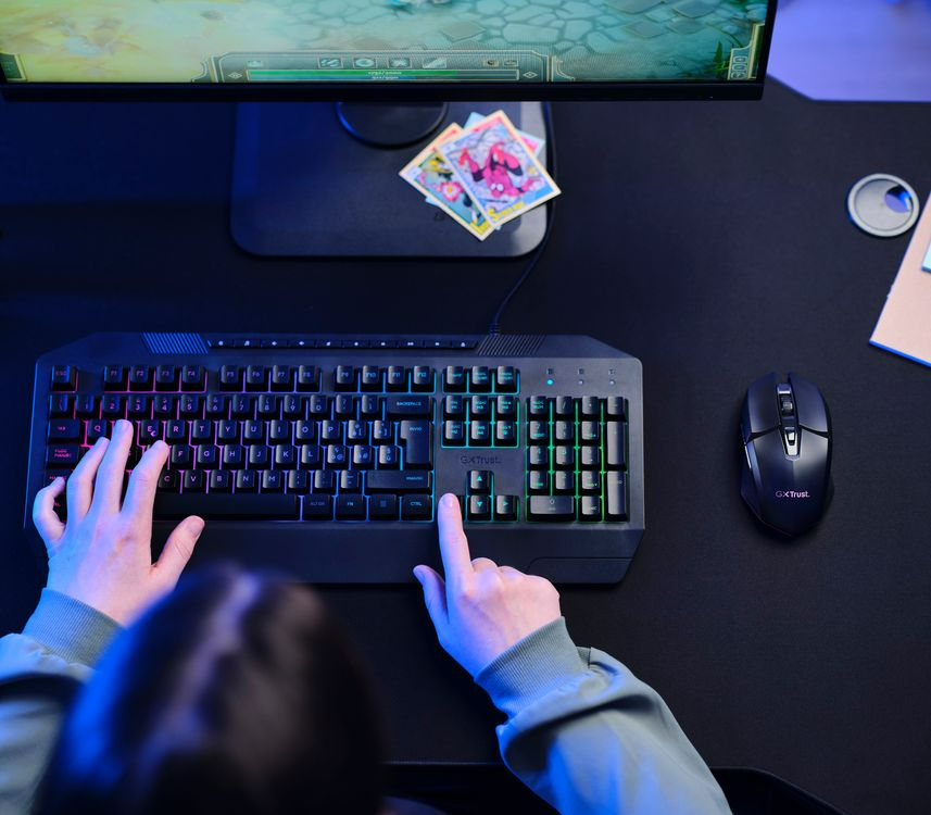 Egy személy kezei egy fekete gamer billentyűzetet és egy egeret használnak egy sötét asztalon.