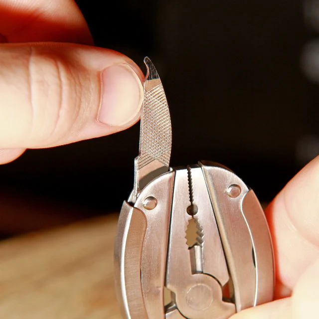 Hand, die ein silbernes Multi-Tool hält, mit teilweise ausgezogener Feile.
