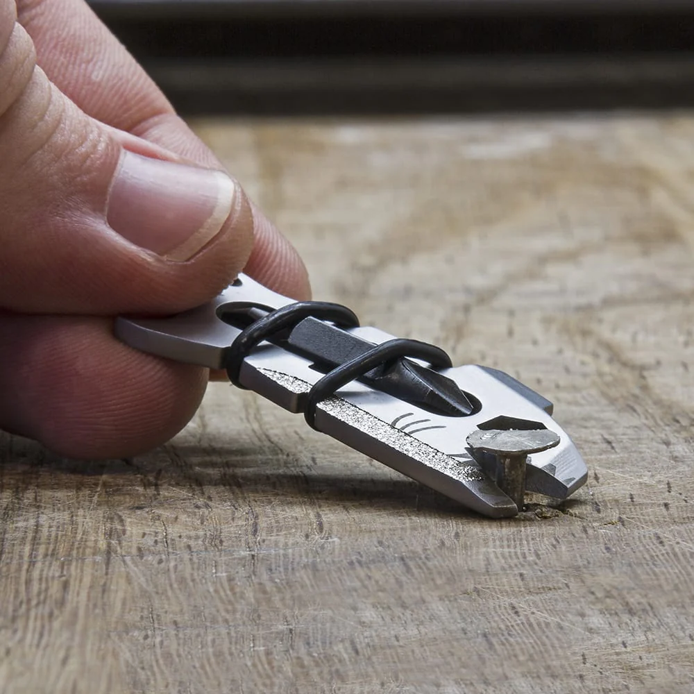 Ein kleines Multitool, das einen Nagel als Werkzeug verwendet. Es liegt auf einer Holzoberfläche.