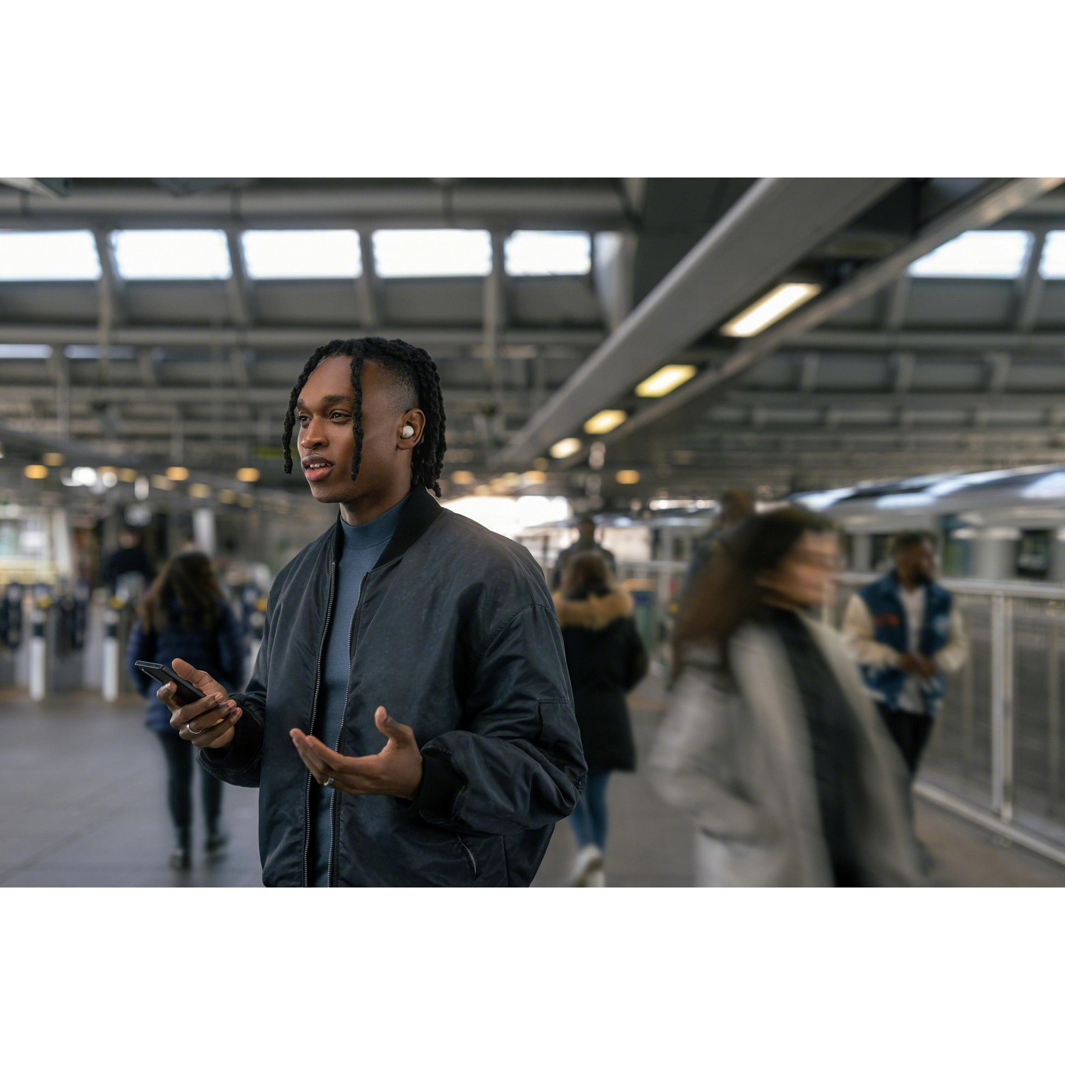 Homme avec des écouteurs dans une gare, tenant un téléphone.