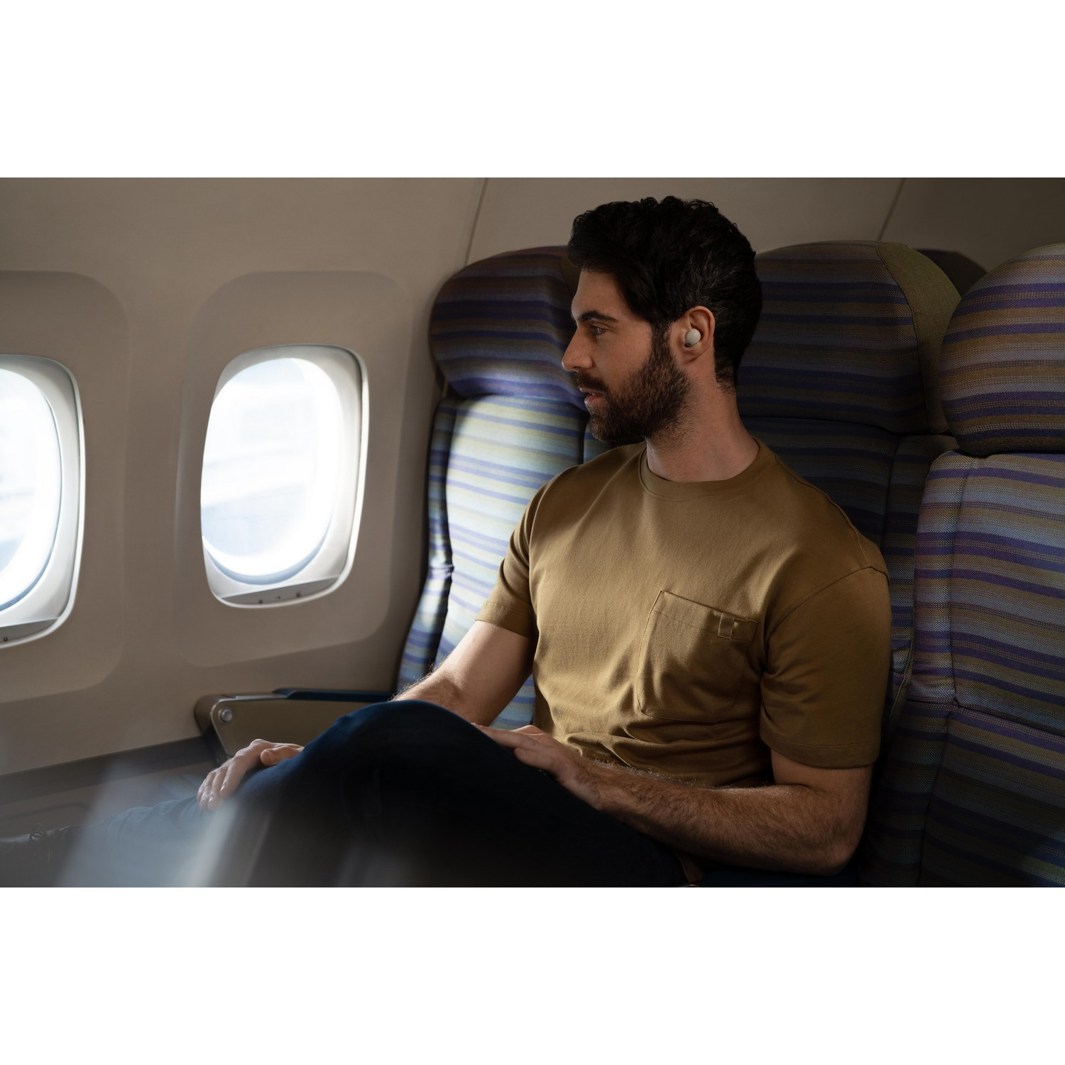 Un homme portant des écouteurs est assis près d'une fenêtre dans un avion, regardant dehors.