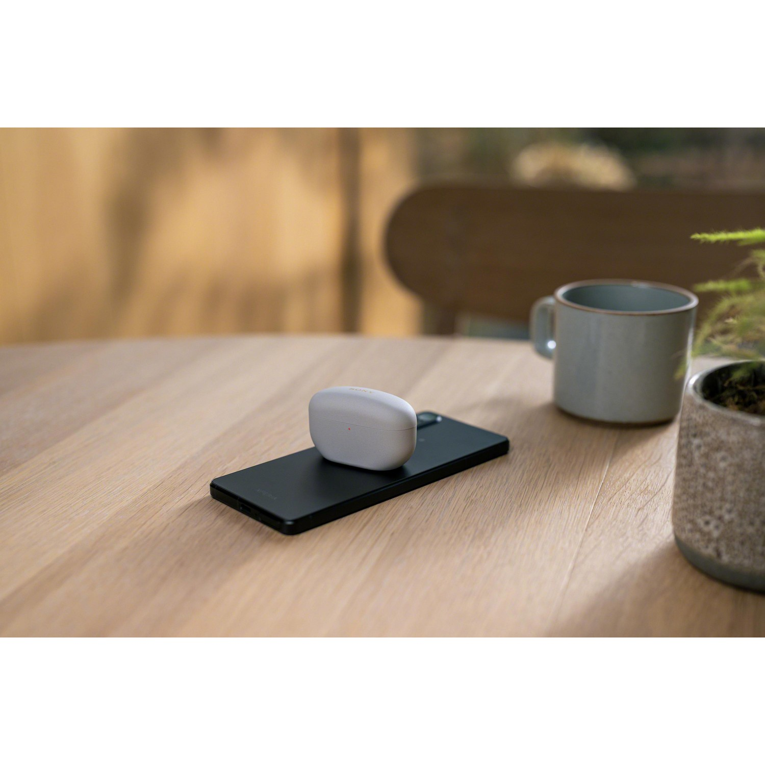 Écouteurs sur un téléphone noir sur une table en bois, avec une tasse et une plante.