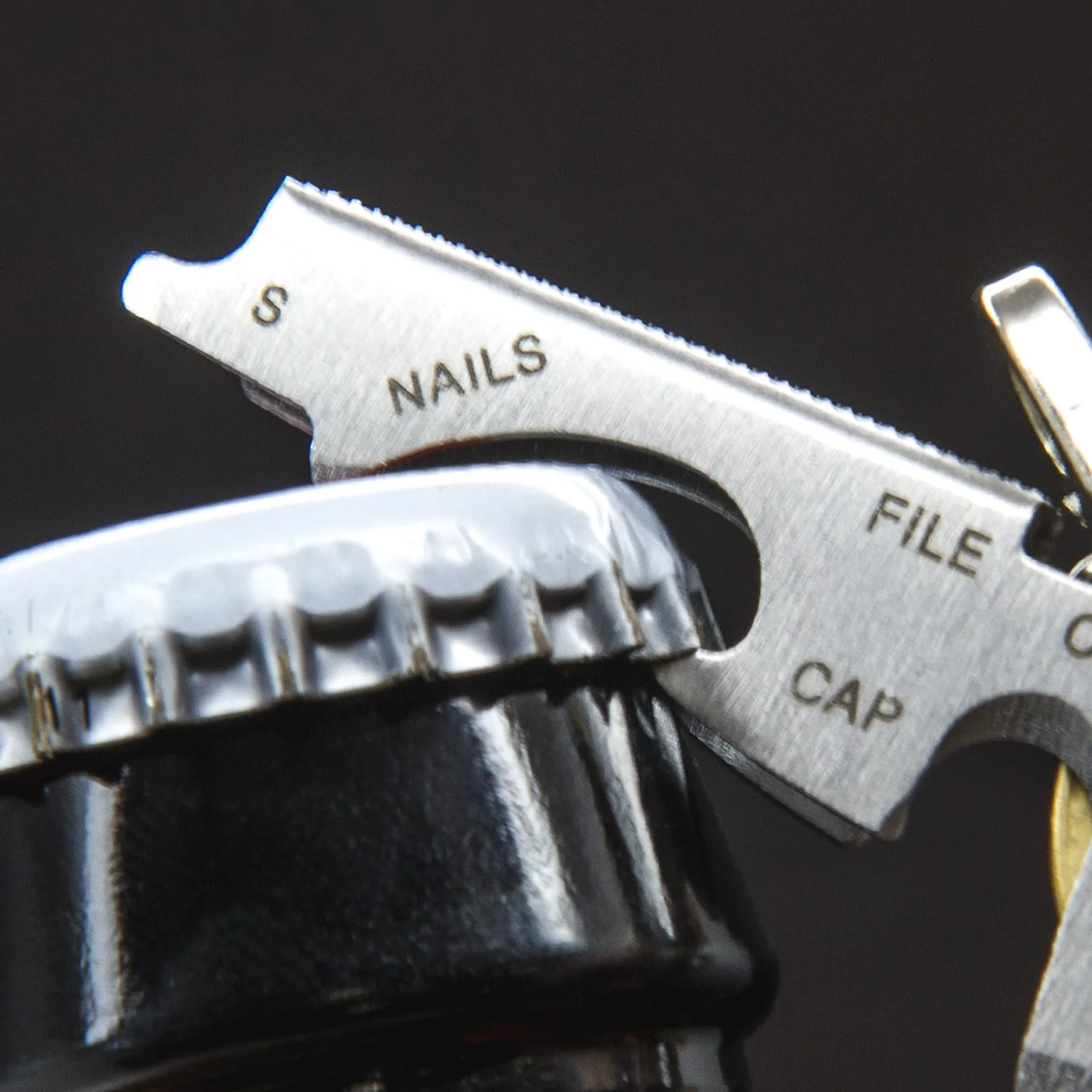 Ein Multitool öffnet eine Flasche. Es hat die Markierungen 'NAILS', 'FILE' und 'CAP'. Der Flaschenverschluss ist schwarz.