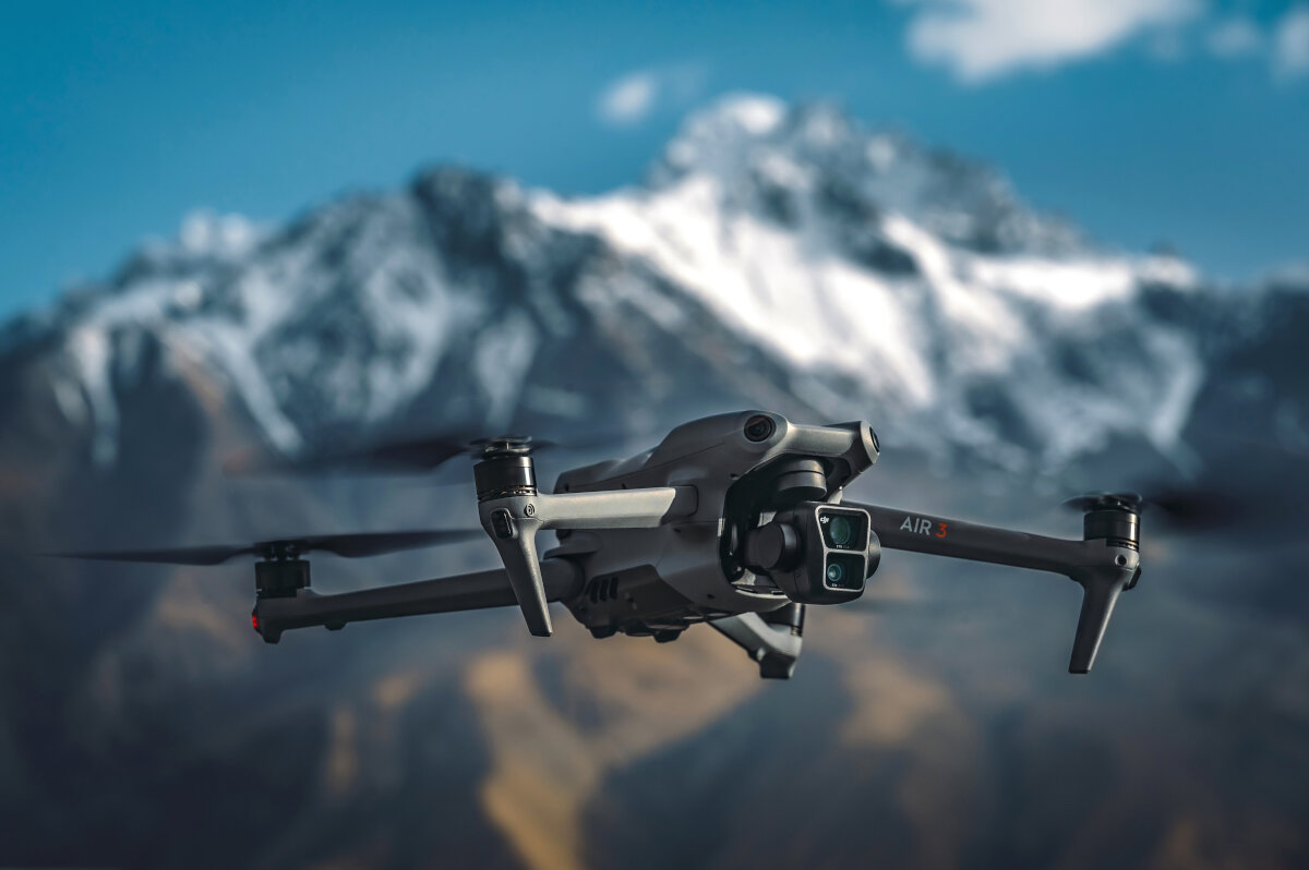 Dron lecący przed ośnieżonym pasmem górskim na tle błękitnego nieba.