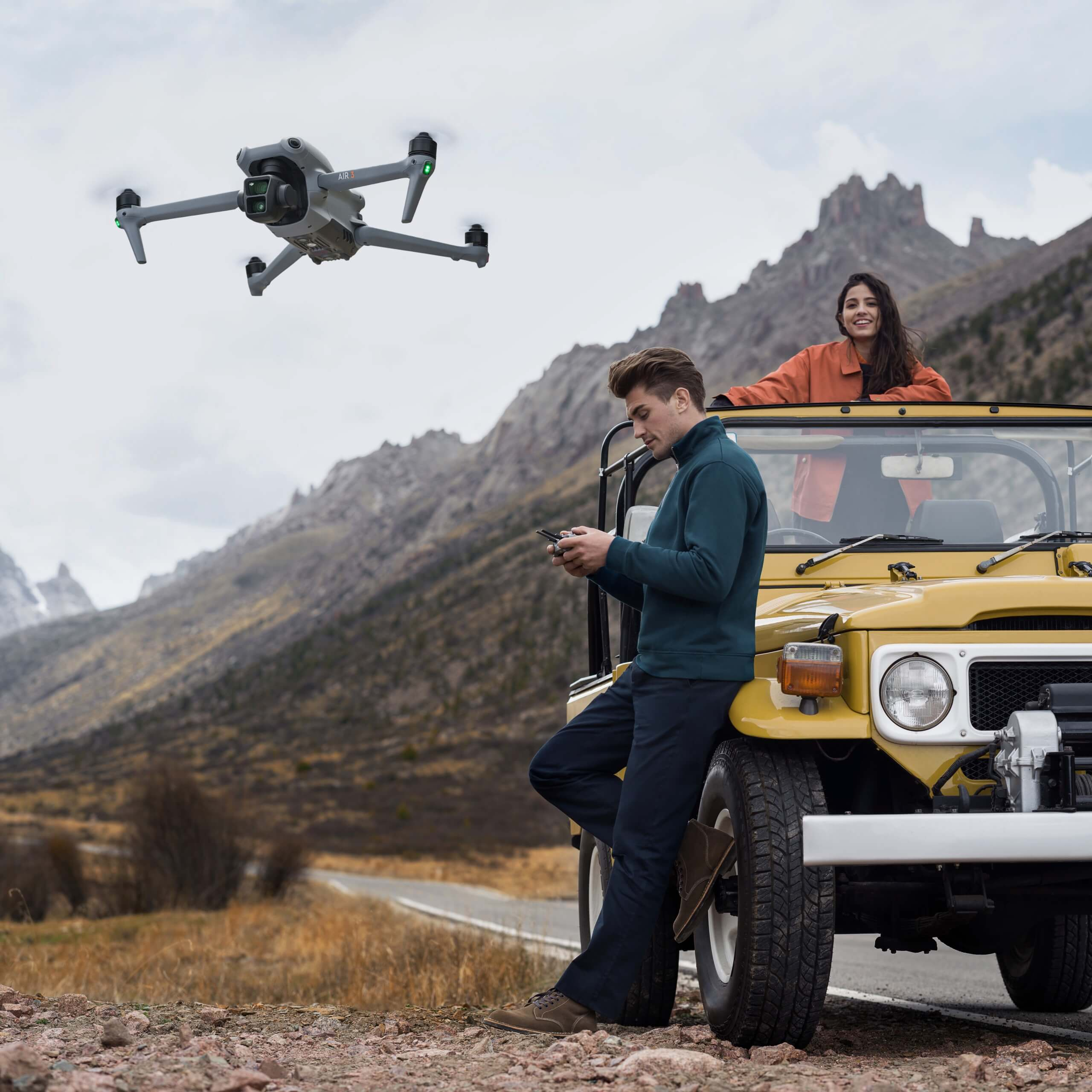 Eine Drohne fliegt über einem gelben Jeep mit einem Paar im Hintergrund.