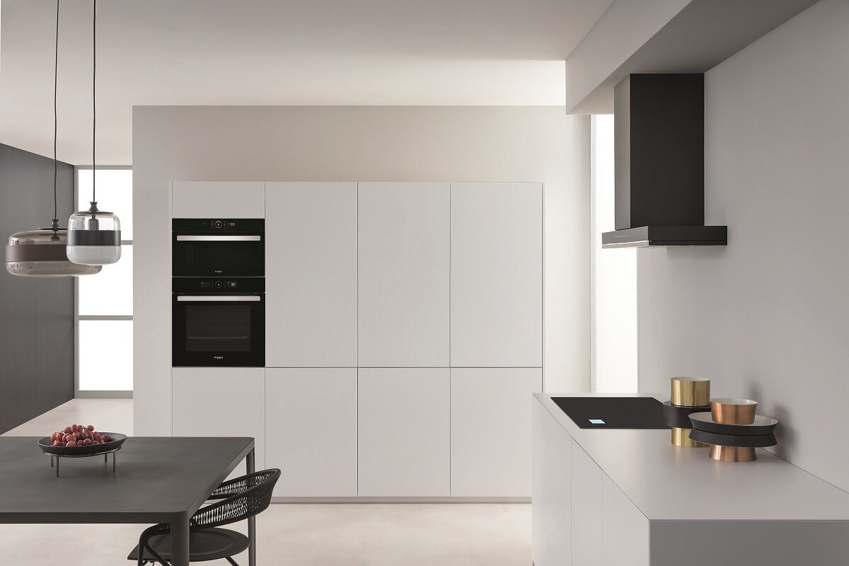 Nowoczesna biała kuchnia z białymi szafkami, piekarnikiem, płytą grzewczą i czarnym okapem.