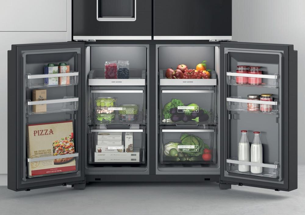 Lodówka z otwartymi drzwiami wypełniona produktami spożywczymi. Przezroczyste szuflady zawierają owoce, warzywa i pakowane produkty.