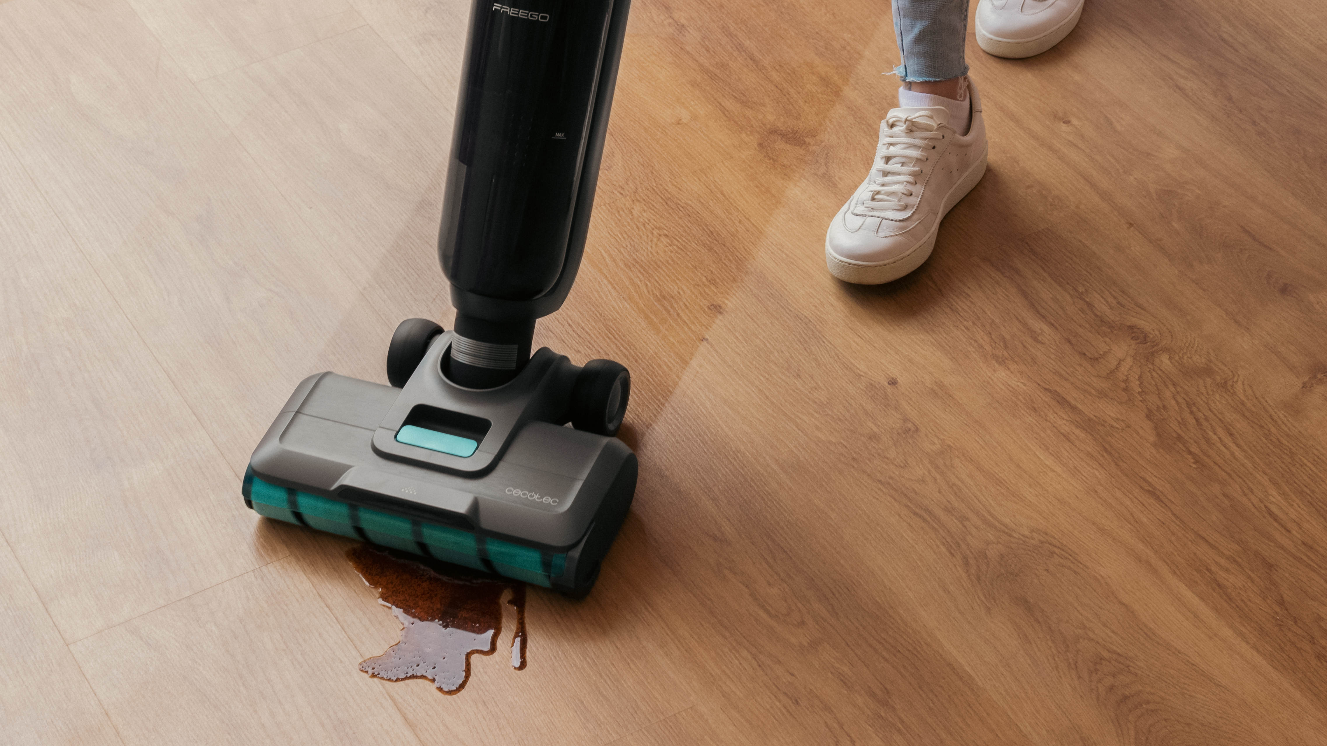 Una persona limpiando un suelo de madera con un limpiador de suelos negro y gris.
