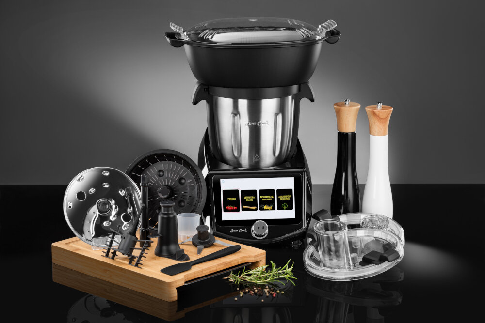 Czarny i stalowy robot kuchenny z akcesoriami na drewnianej desce, czarnym stole i szarym tle.