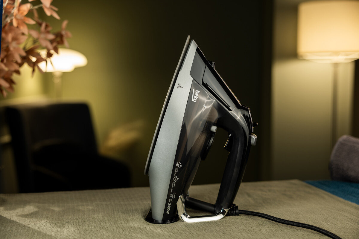 Czarne i szare żelazko na jasnoszarej powierzchni. Tło to ciemne otoczenie.